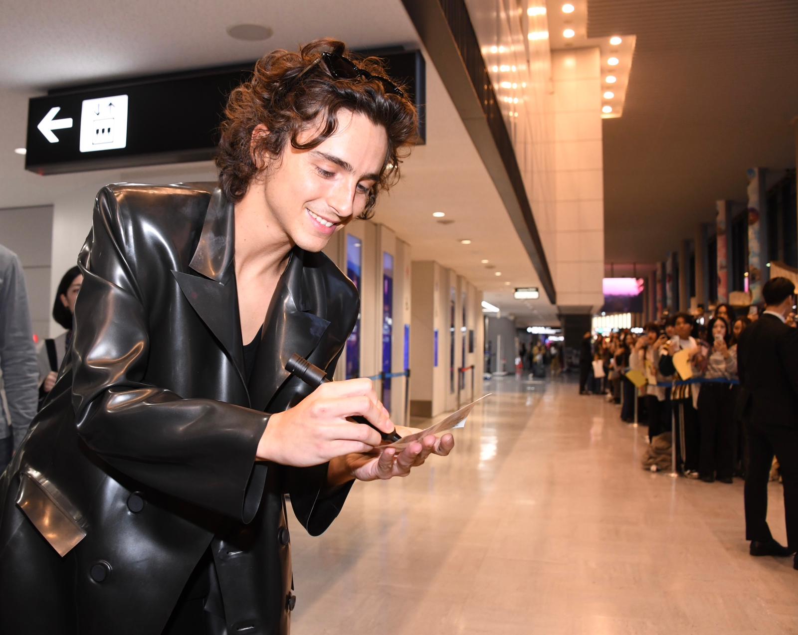 提摩西夏勒梅抵達東京的時候，皮大衣底下僅有穿著黑色背心，似乎對接下來的深V時尚展開預告。（華納兄弟提供）