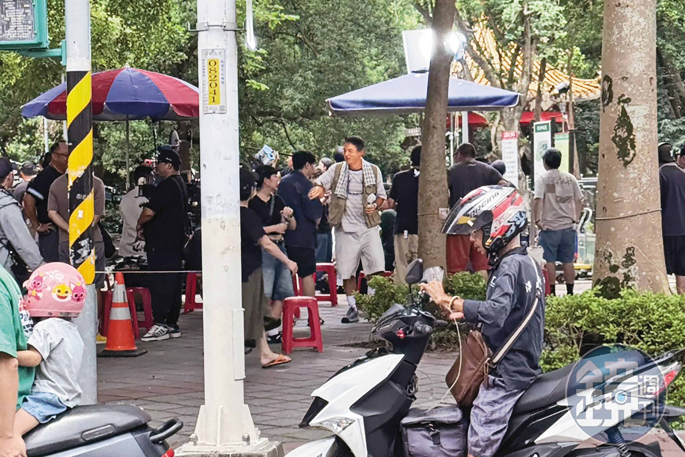 8日中午，李銘順（右）現身新北市永和四號公園一角，他脖子上掛毛巾，手持隨身電風扇，在樹蔭下等候拍攝。