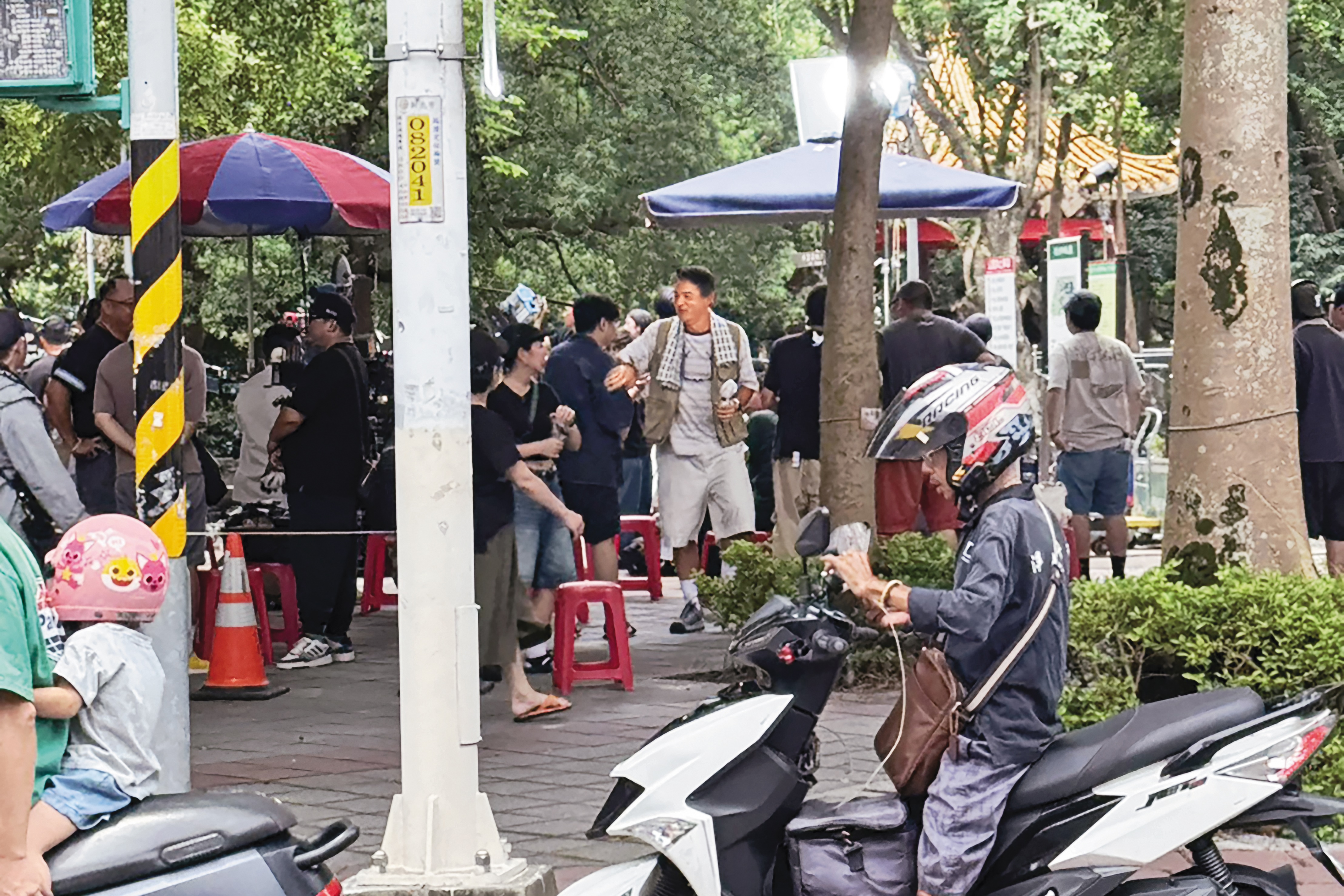 8日中午，李銘順（右）現身新北市永和四號公園一角，他脖子上掛毛巾，手持隨身電風扇，在樹蔭下等候拍攝。