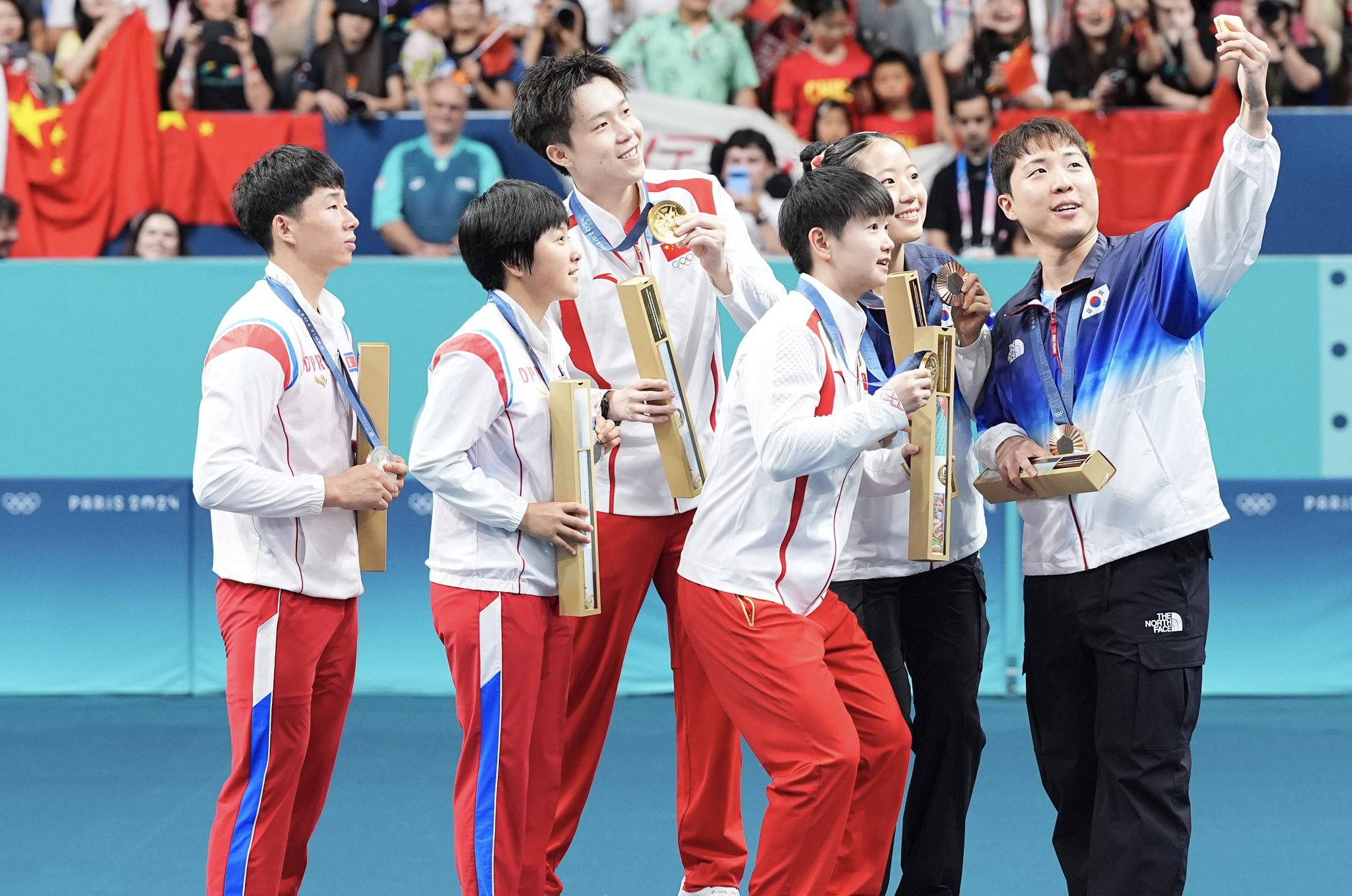 日前桌球混雙賽事中，南韓選手與奪金的中國隊、摘銀的北韓隊拍團體照，該自拍照在網路引起熱議。（翻攝自X@SpokespersonCHN）
