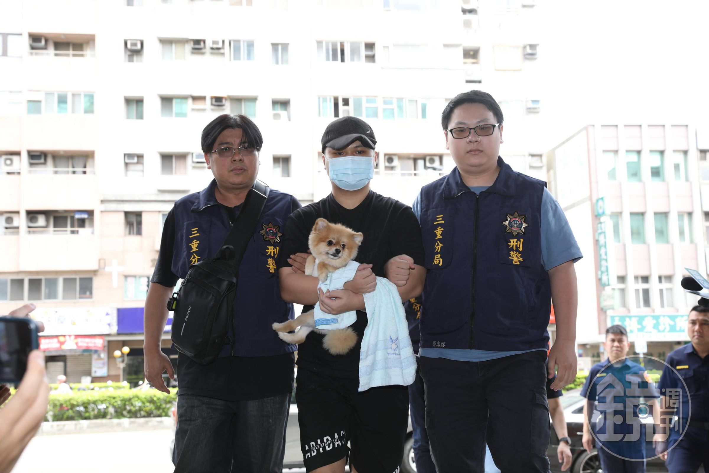 犯下三重滅門血案的張姓男子（中）今日被移送至警局時，懷中緊抱寵物犬。