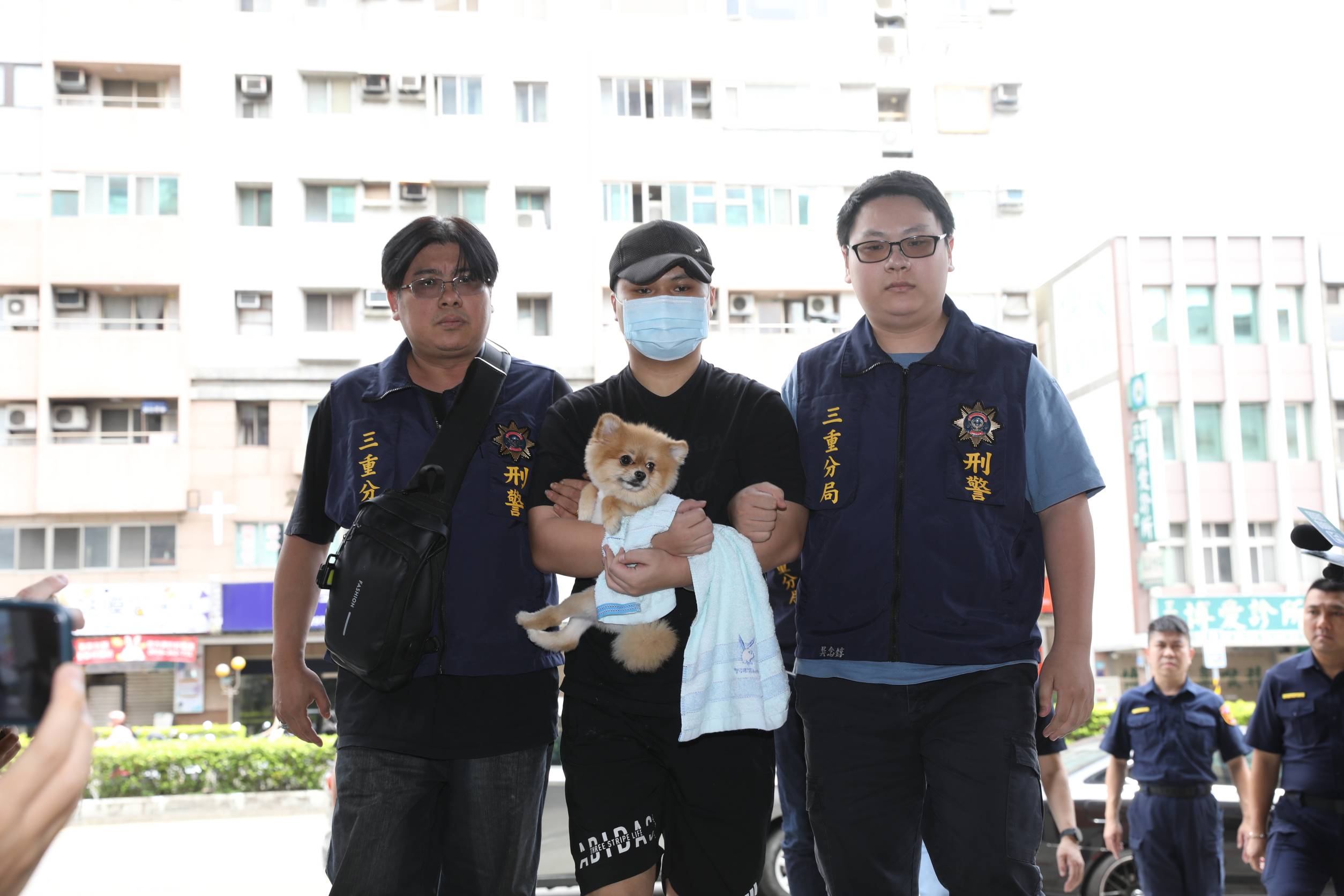 犯下三重滅門血案的張姓男子（中）今日被移送至警局時，懷中緊抱寵物犬。