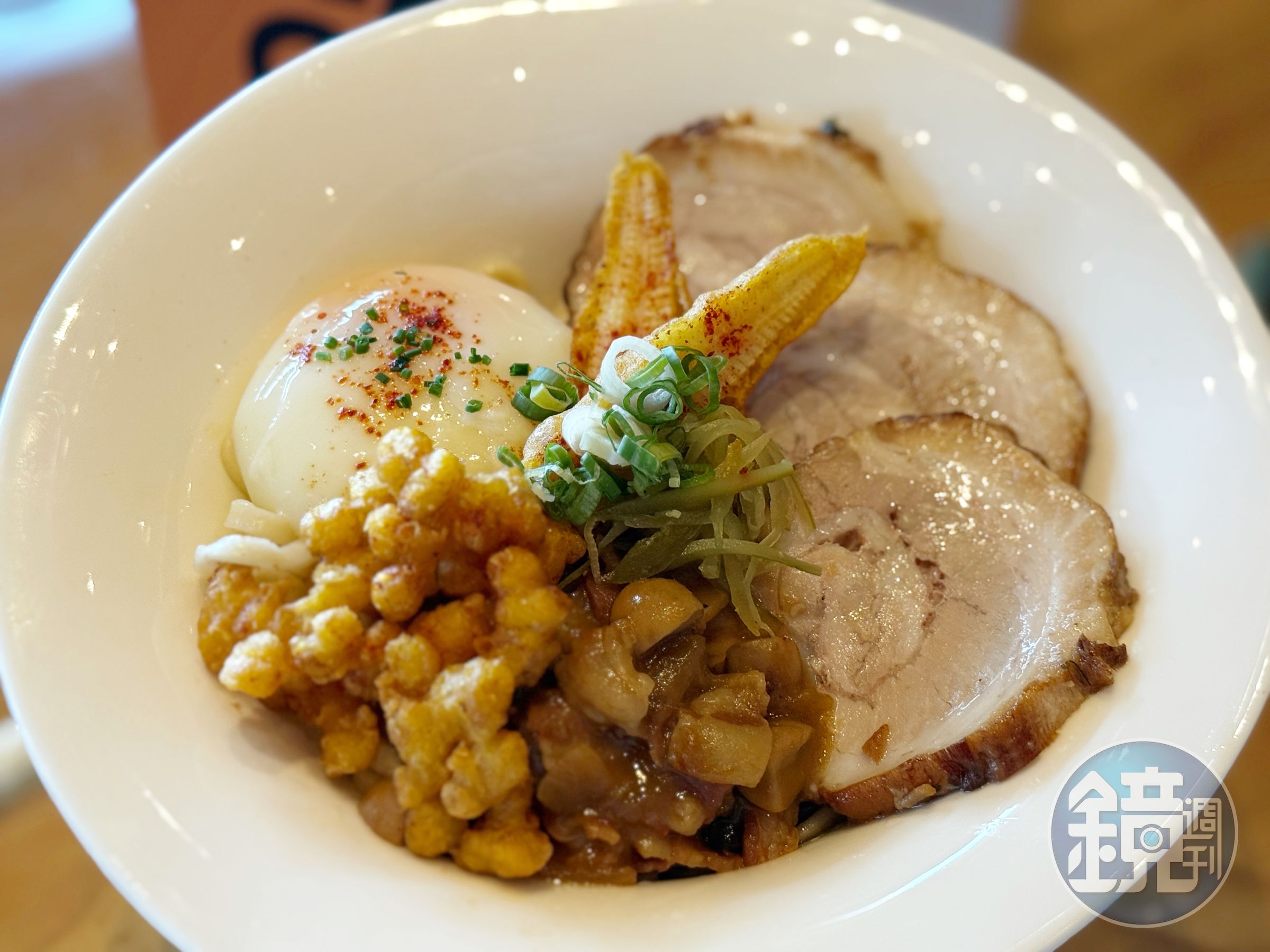 「焦香叉燒湯麵」配料炸玉米筍的麵衣中以印度香料瑪薩拉提味，另備清爽的酸黃瓜，推薦吃法是在湯中拌開溫泉蛋。（428元／碗）