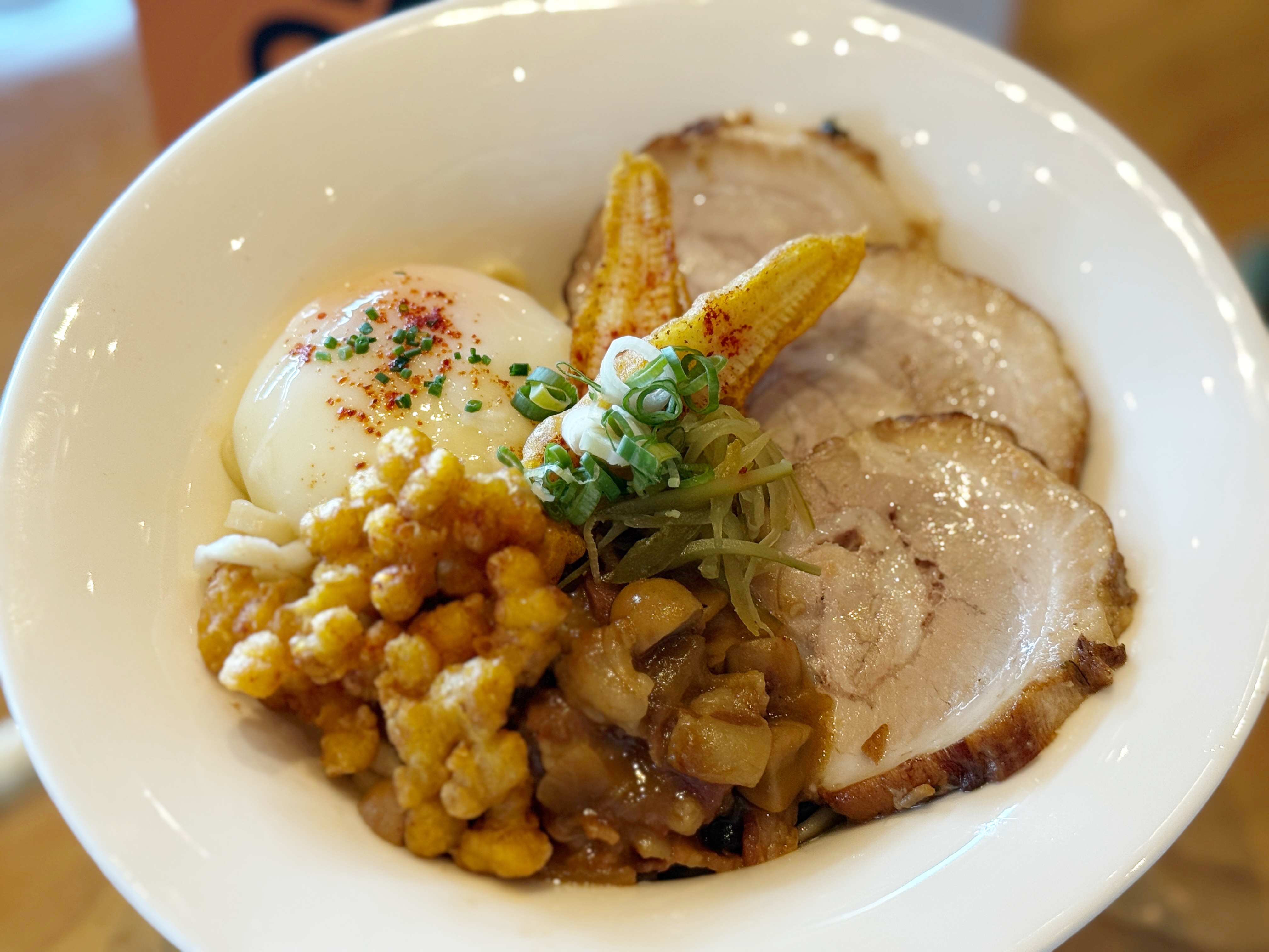 「焦香叉燒湯麵」配料炸玉米筍的麵衣中以印度香料瑪薩拉提味，另備清爽的酸黃瓜，推薦吃法是在湯中拌開溫泉蛋。（428元／碗）