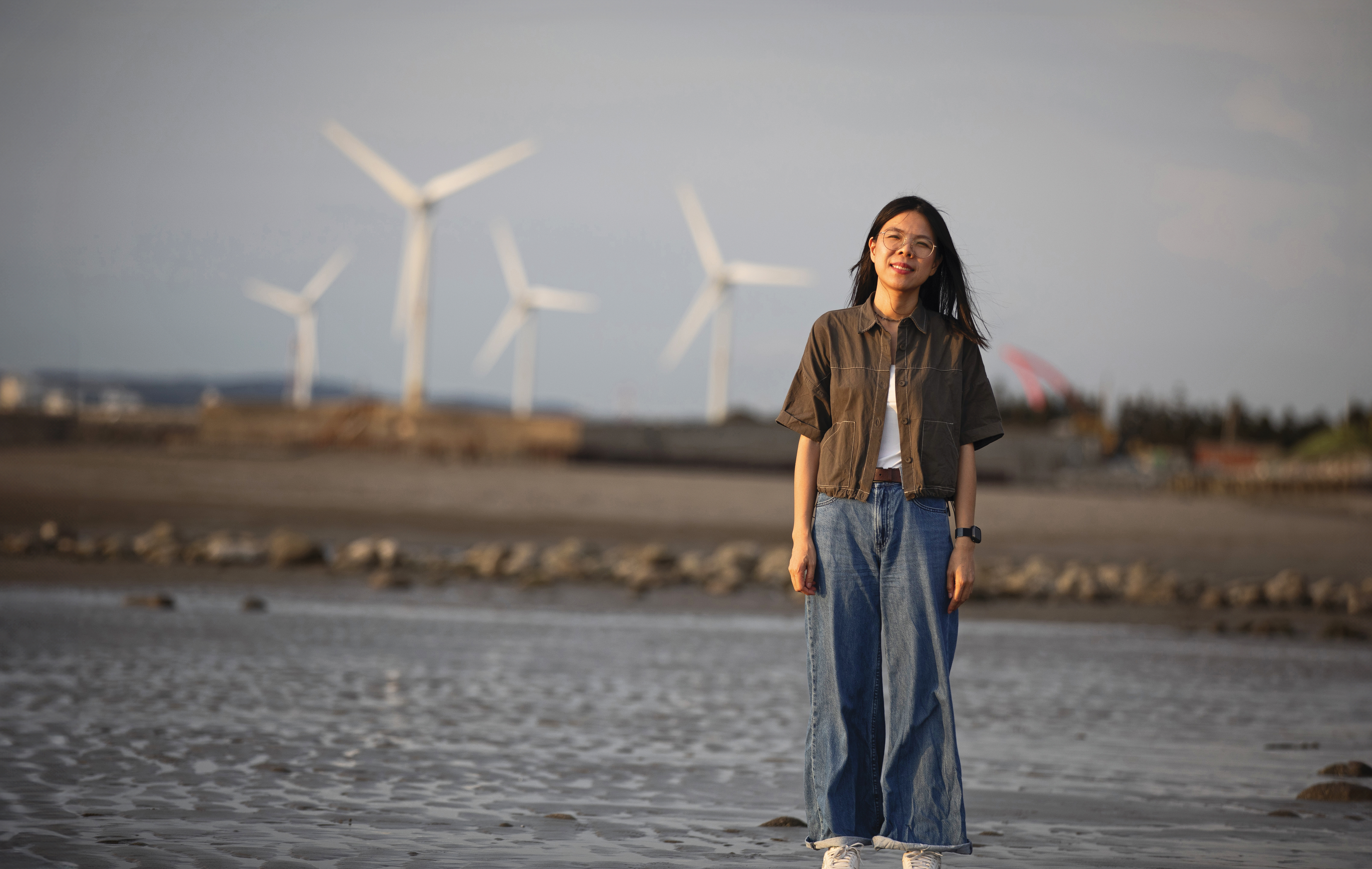 劉育育在苑裡海邊，遠處有風力發電機組，是濱海鄉鎮常見風景。