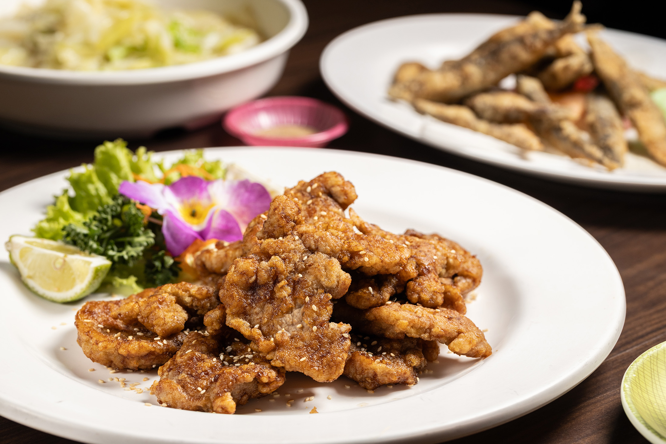 「醬燒菲力豬」（前，250元／份）選用豬腰內肉製作，肉質細嫩不乾柴，搭配店內自熬醬汁，鹹甜平衡；「鹽酥喜相逢」（右後，150元／份）挑選魚蛋飽滿的大尾魚隻，高溫油炸後外酥內嫩、是不少熟客必點的下酒菜。