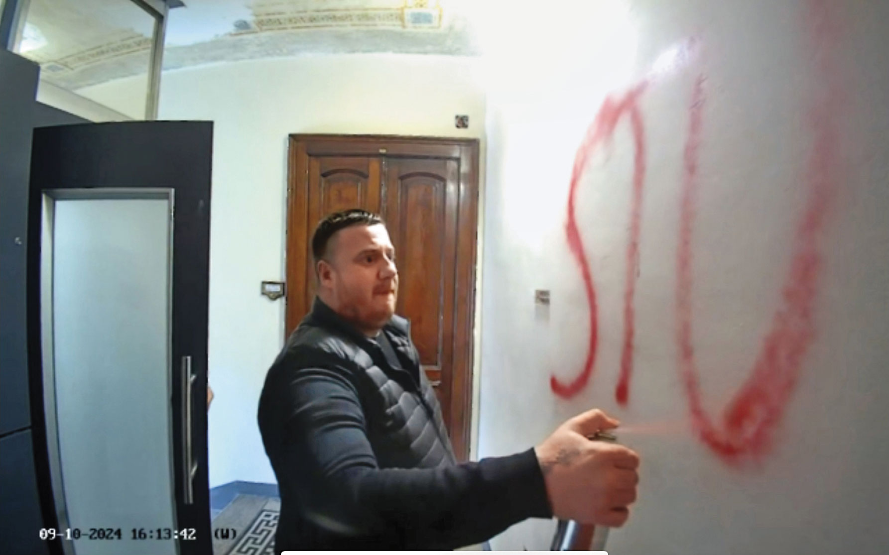 李穎家門口的監視器錄下噴漆者，此人噴完牆面，數秒後將監視鏡頭也噴成紅色。左側門後當時還藏有另一人。（李穎提供）