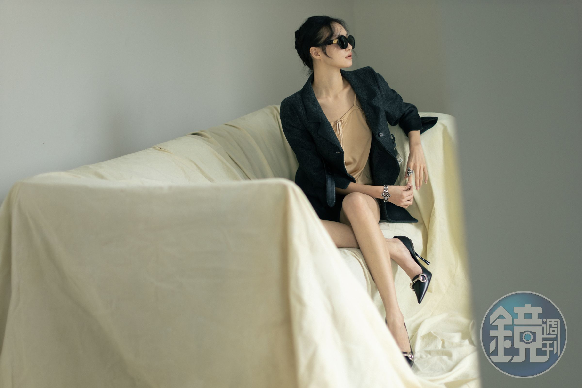 膚色內裡綁帶洋裝 價格店洽 by MIU MIU；灰色造型外套 價格店洽 by MIU MIU；黑色高跟鞋 價格店洽 by GUCCI；黑色墨鏡 NT$14,250 by LOEWE；水晶裝飾戒指 價格店洽 by GUCCI；水晶裝飾手鍊 價格店洽 by GUCCI。