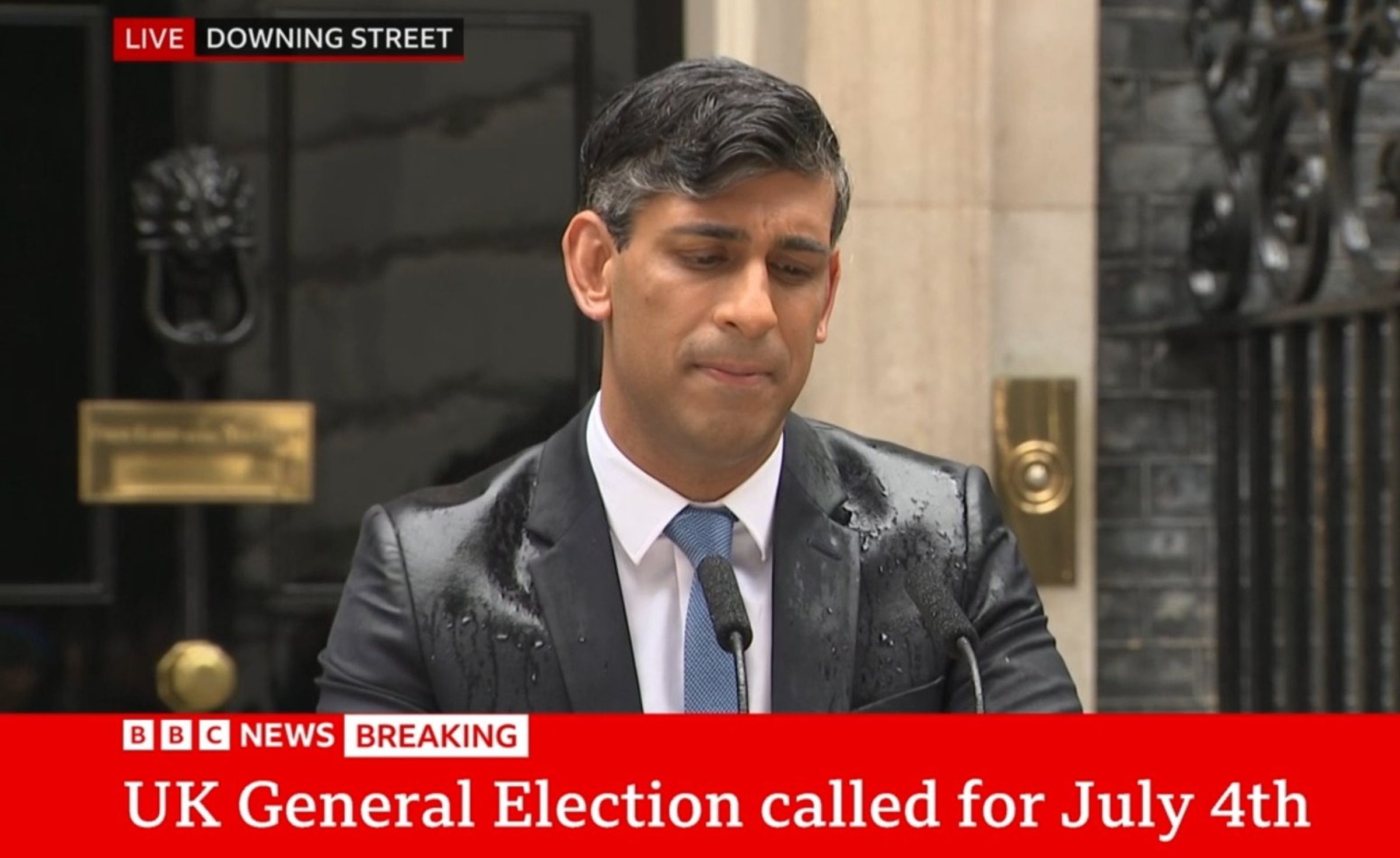 英國首相蘇納克在首相府前淋雨,宣布7月4日舉行大選。(翻攝BBC畫面)
