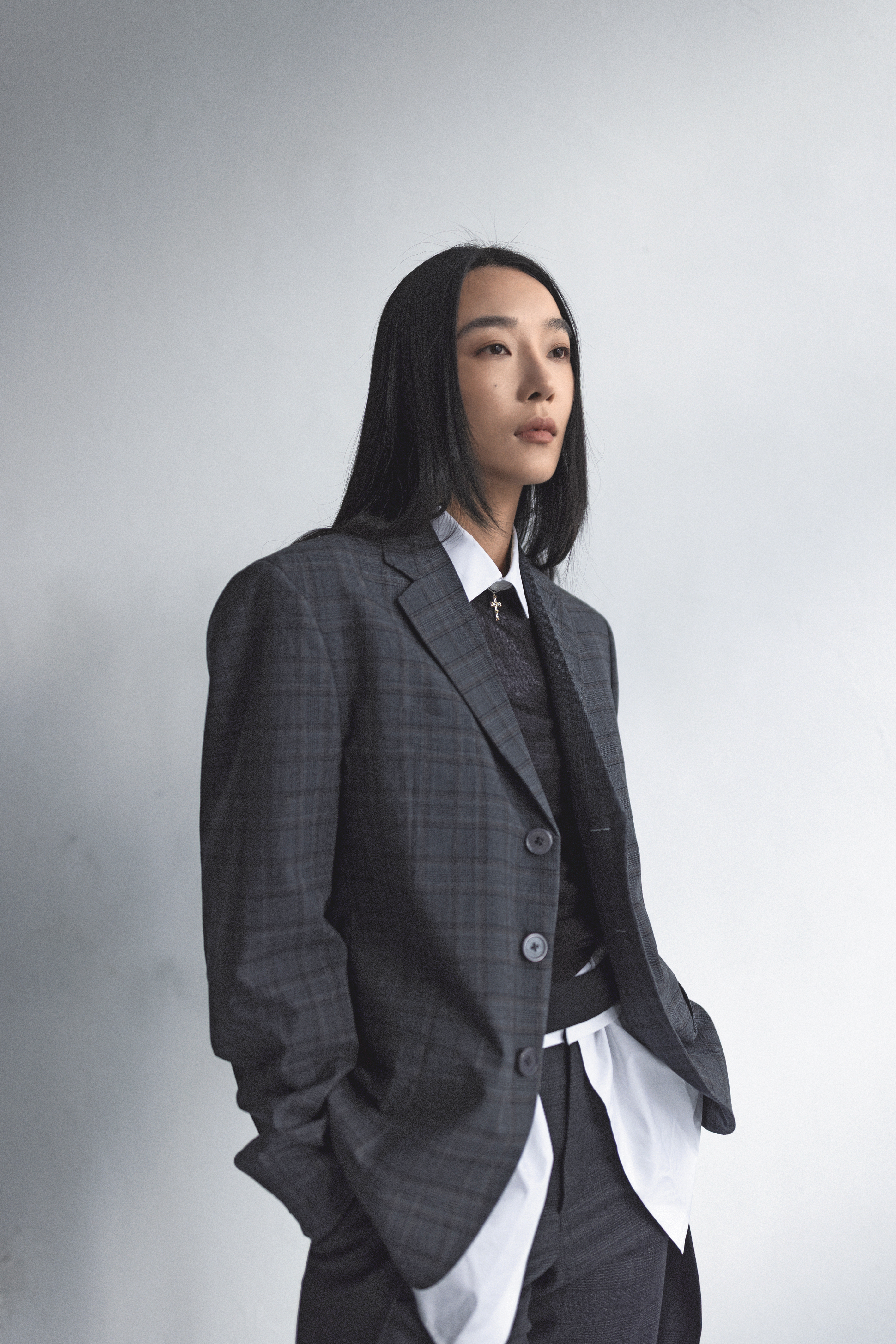 格紋羊毛外套 價格店洽 by Prada；咖啡色針織衫 價格店洽 by Prada；棉質撞色襯衫 價格店洽 by Prada；灰色長褲 價格店洽 by Loewe；十字架項鍊 價格店洽 by Tiffany & Co.。