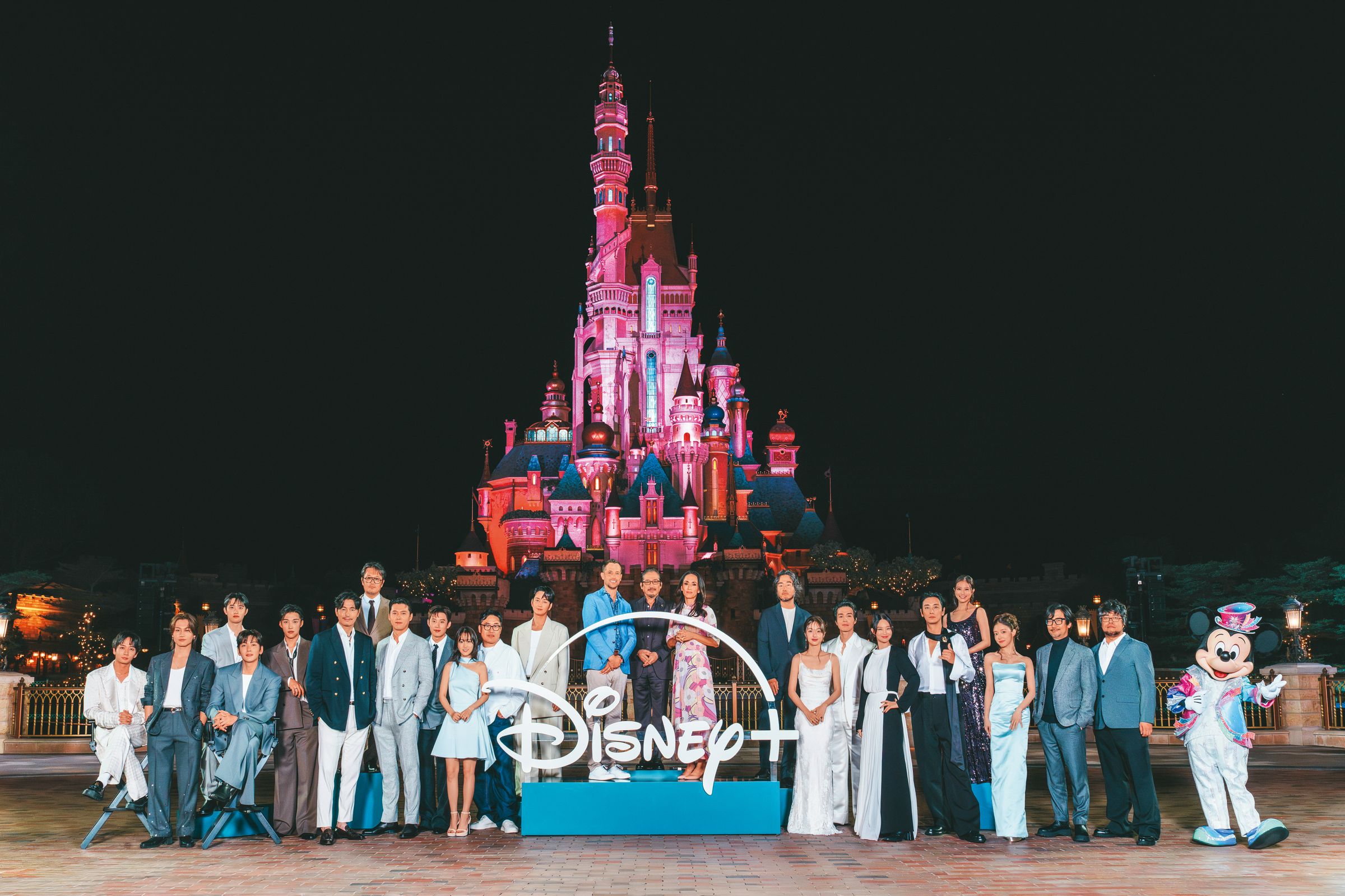 Disney+原創內容發布會今年移師至香港迪士尼度假區舉行，參與原創作品的日、韓、美影人在園區內城堡前與米奇留影。（Disney+提供）