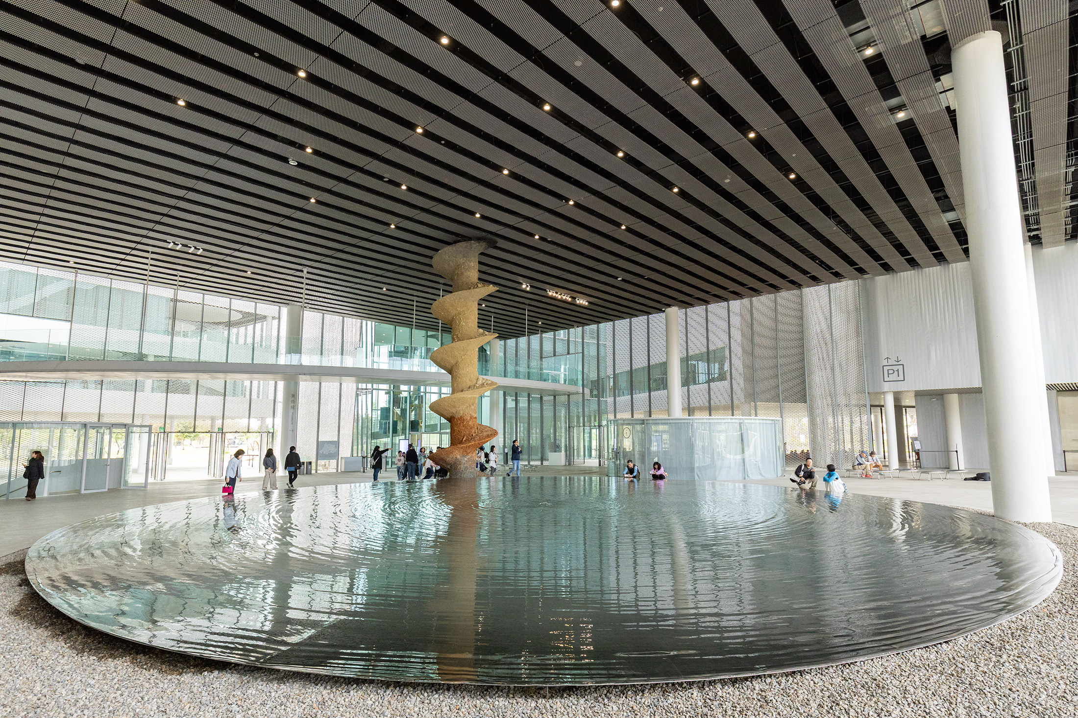 「台中綠美圖」大廳中央的不鏽鋼鏡面水池不僅能反映周圍景色，還能調節大廳溫度；後方是比利時藝術家阿德里安提爾提奧的作品《後博物館證據（探鑽）》。