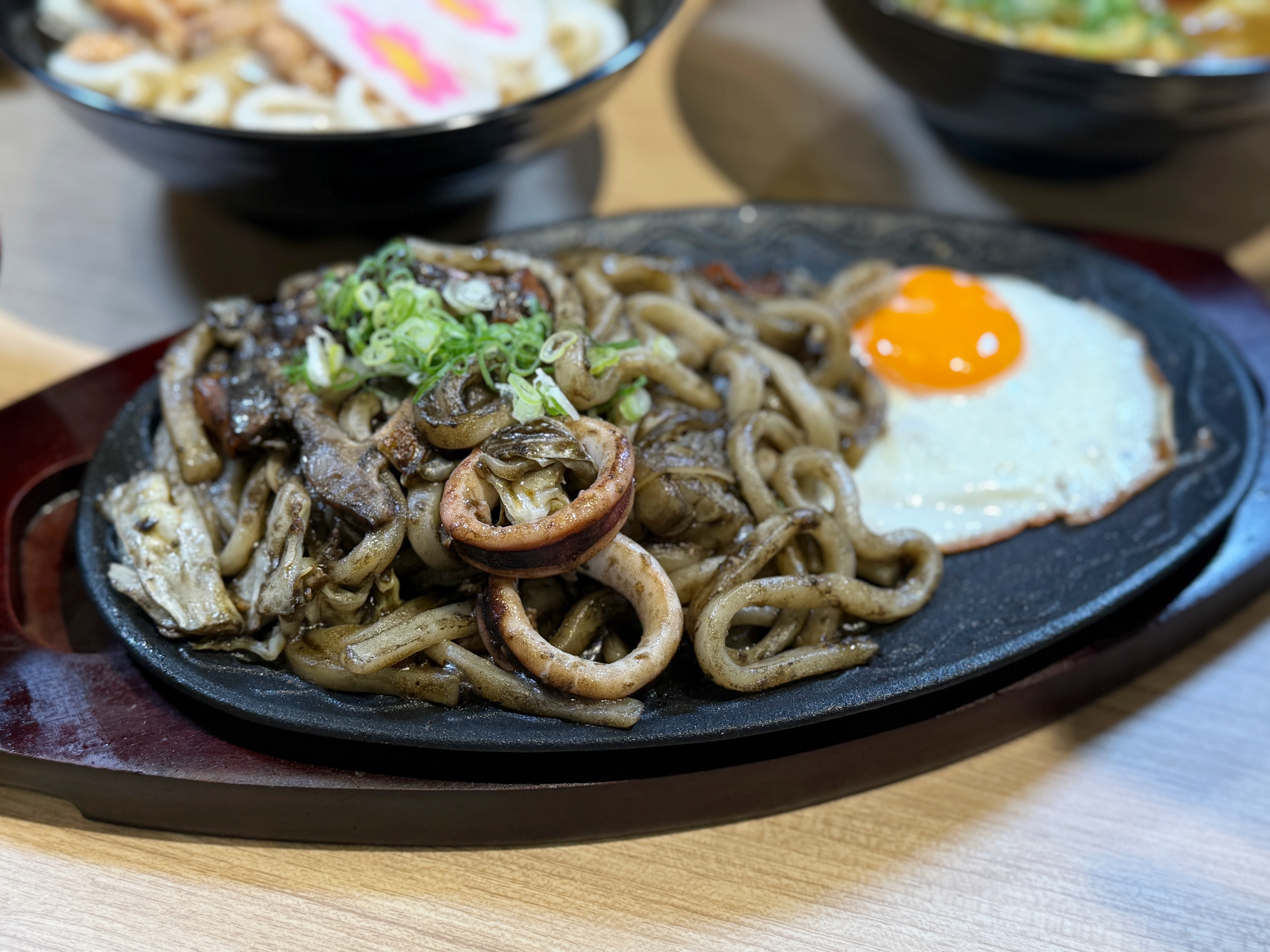台灣限定的「烏賊墨炒烏龍麵」以滾燙鐵板盛裝，濃郁墨魚醬均勻包覆麵條，高溫快炒逼出十足鑊氣，Q彈有勁、越嚼越香。（250元／份）
