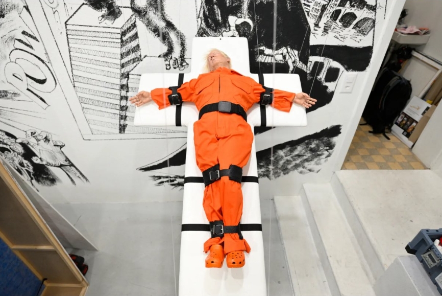 英國藝術家梅森・史托姆創作的《聖人還是罪人》，將川普以橘衣囚犯造型釘上十字架，引發宗教與政治雙重爭議。（翻攝自X/ Manuel Cadonau）