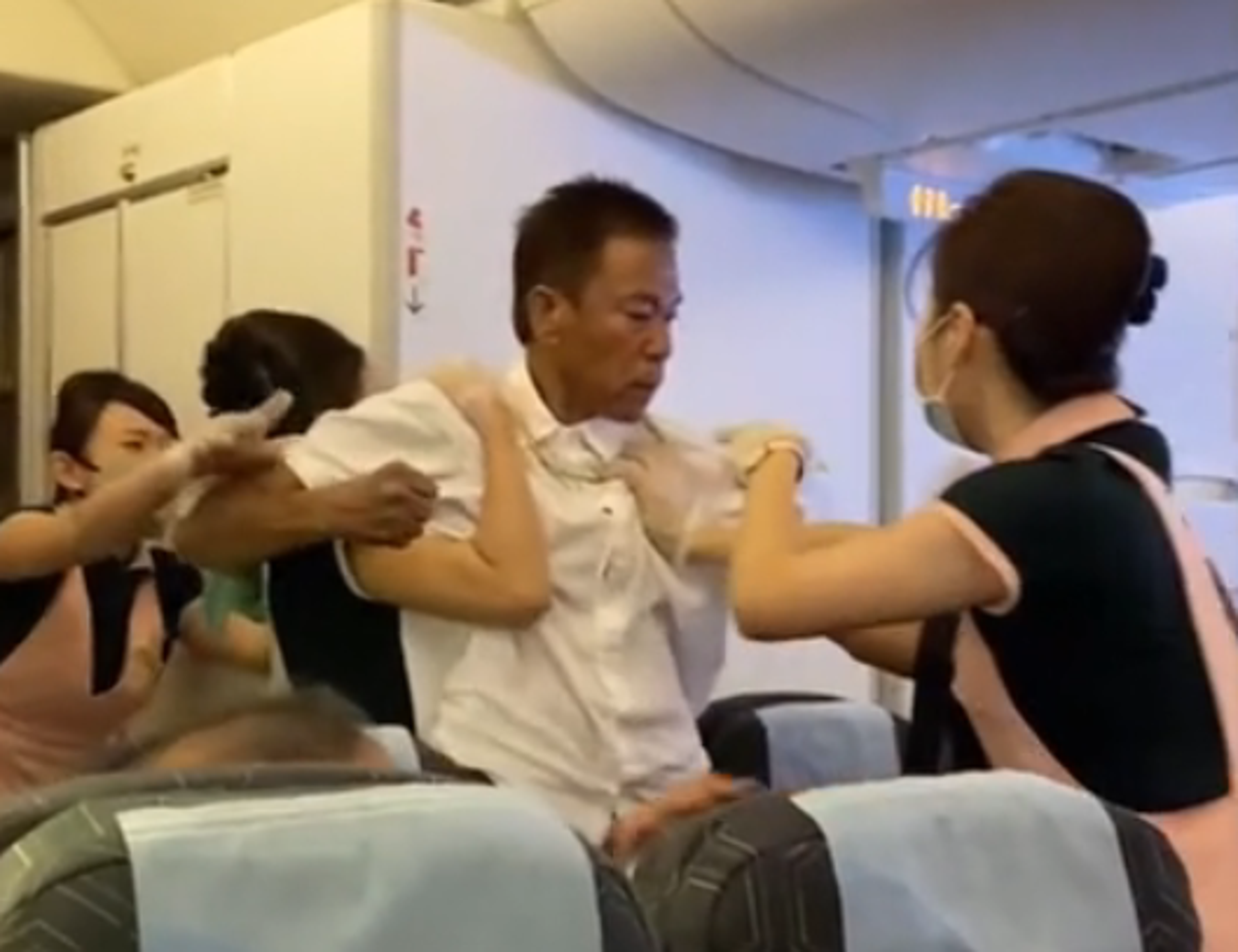 白衣男子與其他乘客爆發肢體衝突，空姐急忙勸架。（翻攝影片畫面）