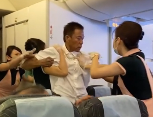 白衣男子與其他乘客爆發肢體衝突，空姐急忙勸架。（翻攝影片畫面）