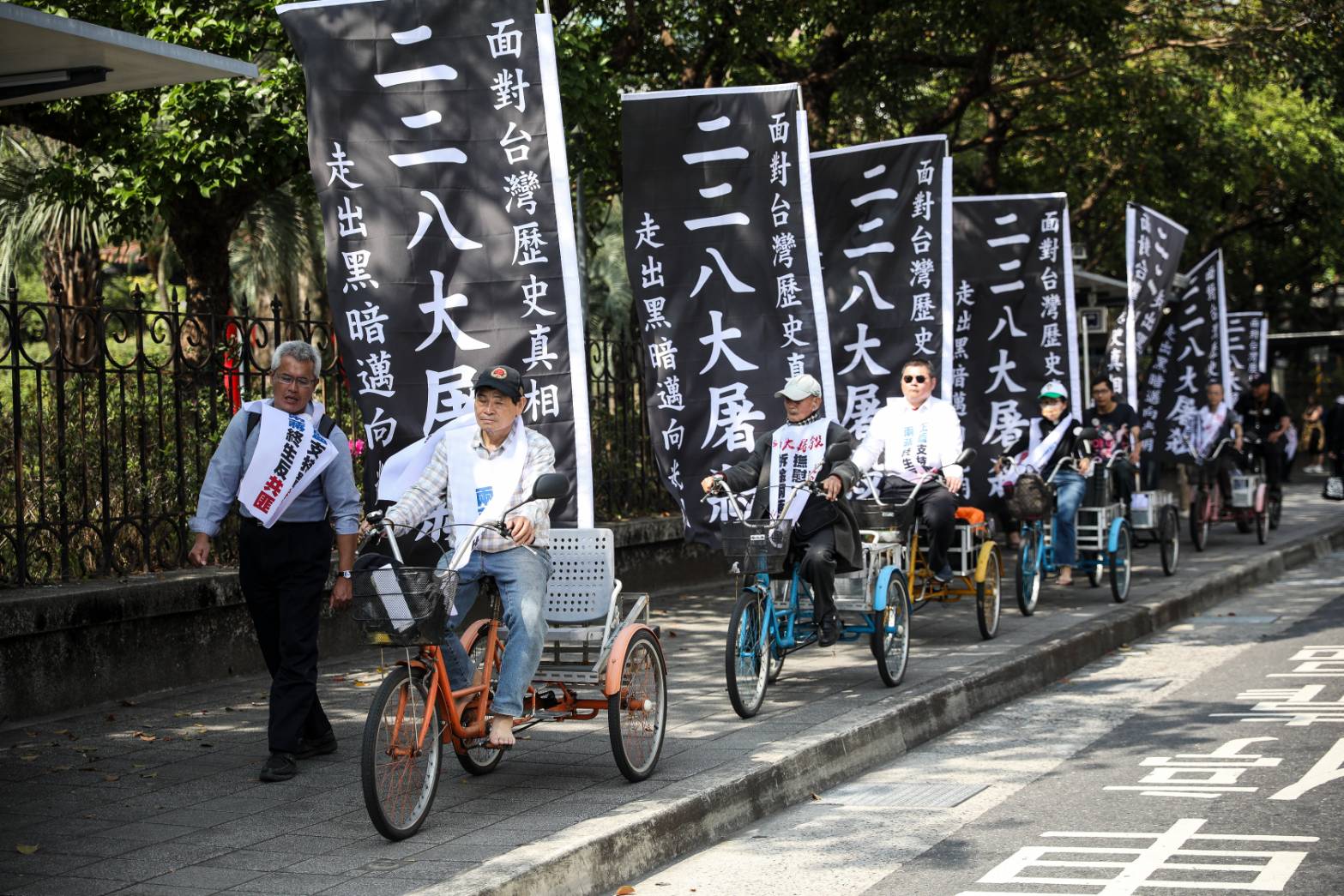 228事件78週年追思會，抗議團體在腳踏車上插著大大的「二二八大屠殺，面對台灣歷史真相，走出黑暗邁向光明」黑底白字布條。