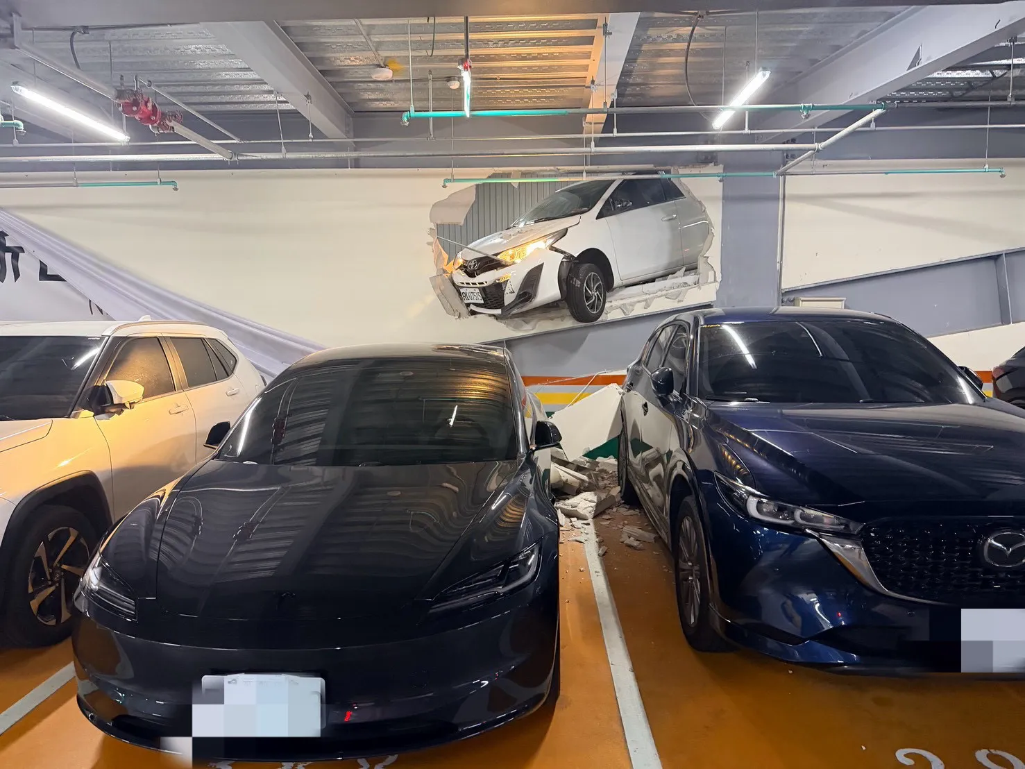 藍男駕駛的車輛突失控撞破牆壁，碎屑石塊波及包括特斯拉在內的３輛車子受損。（翻攝畫面）
