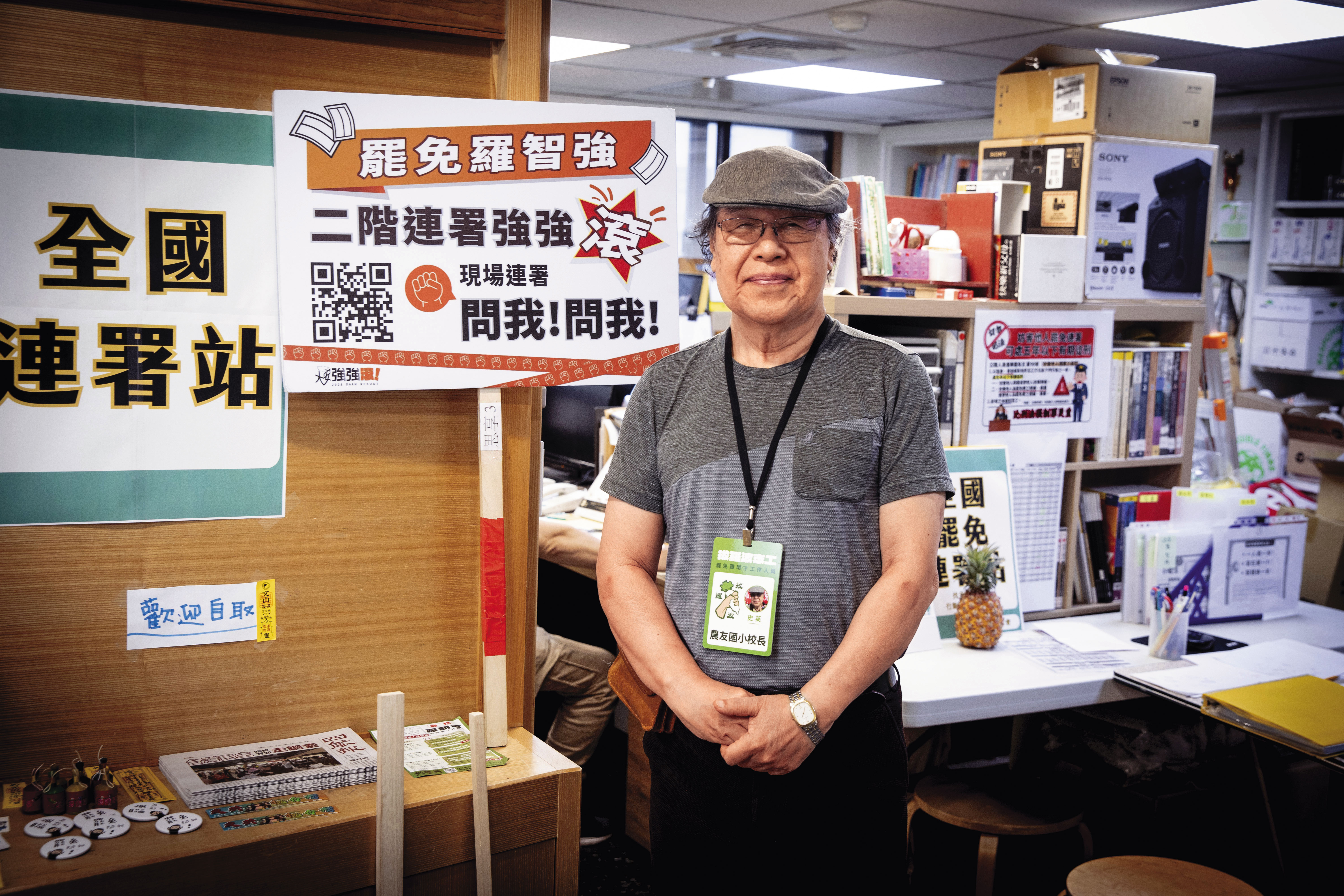 人本教育基金會門口擺滿各類創意貼紙、文宣。圖為史英在台北人本辦公室接受訪談，胸前掛著罷免羅明才的拔羅波志工名牌。