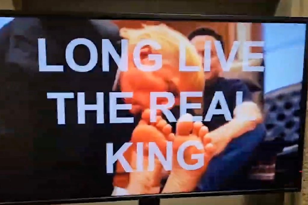 「川普跪舔馬斯克腳」男男片被瘋傳，美政府大樓遭駭客入侵無限播放。（翻自X平台）