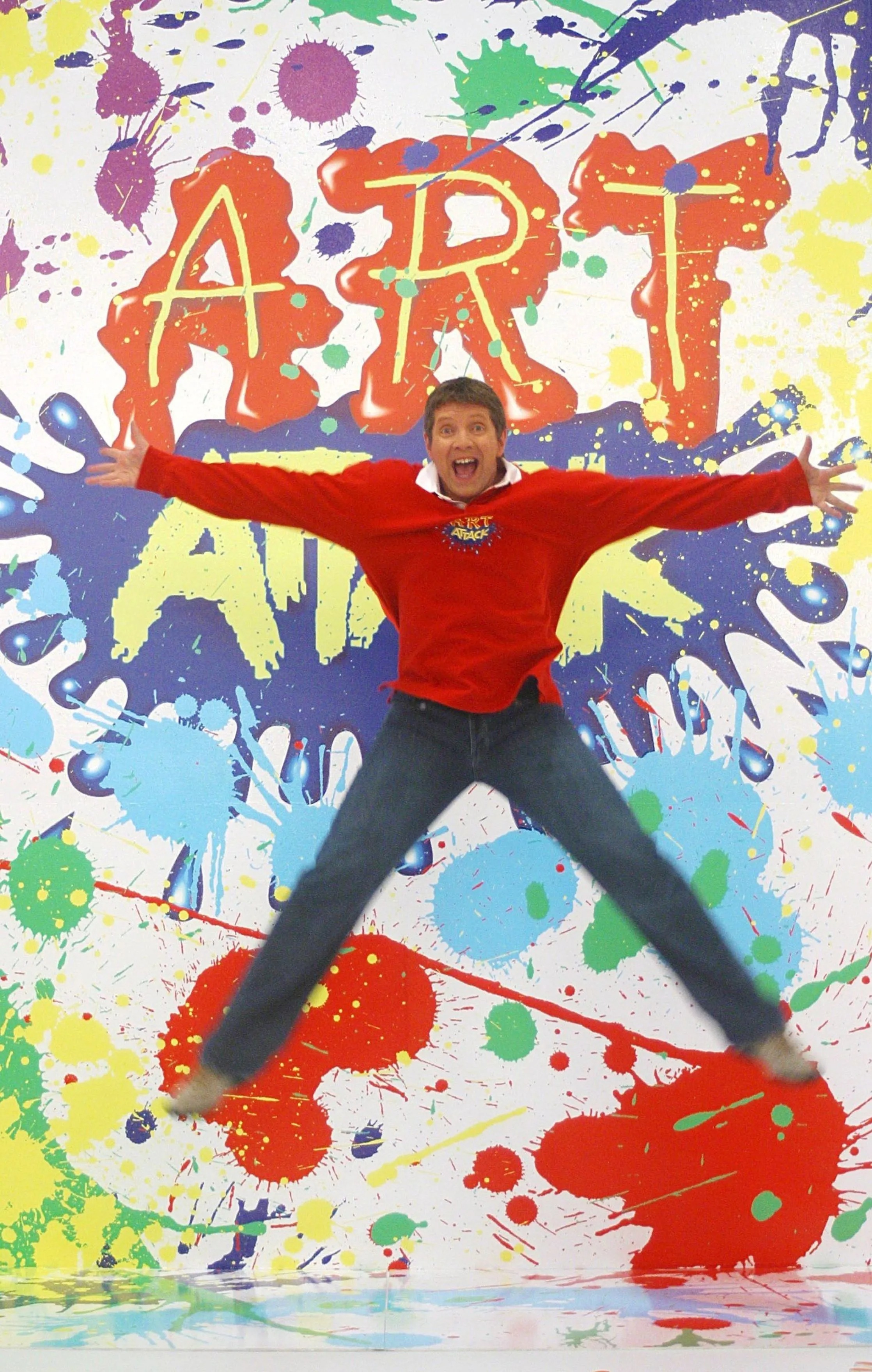 尼爾在《動手玩創意》節目中的招牌動作，背景潑墨與「ART ATTACK」字樣成為一代人難忘畫面。（翻攝ITV）