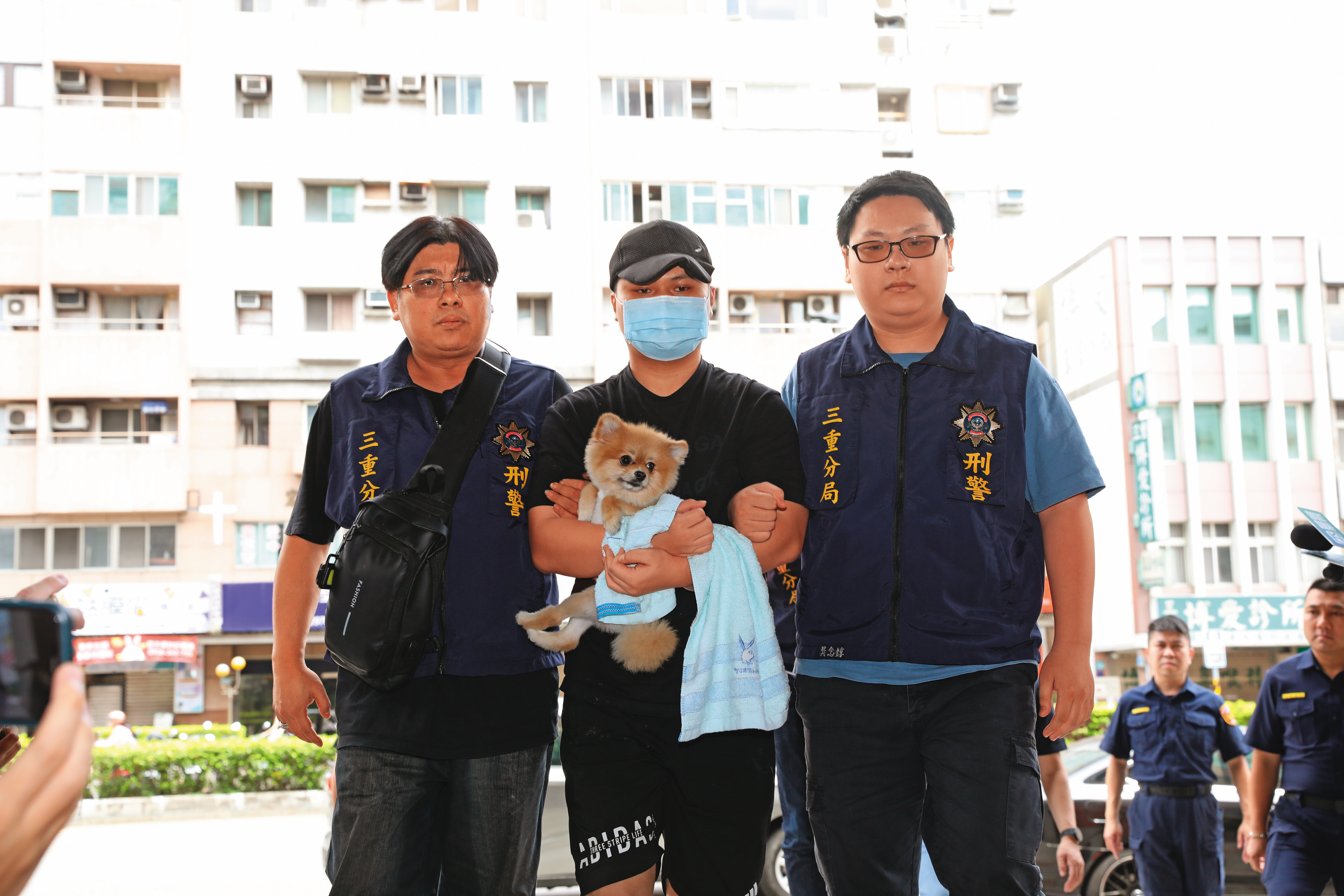張姓嫌犯（中）被上銬帶回警局，手中還抱著愛犬。