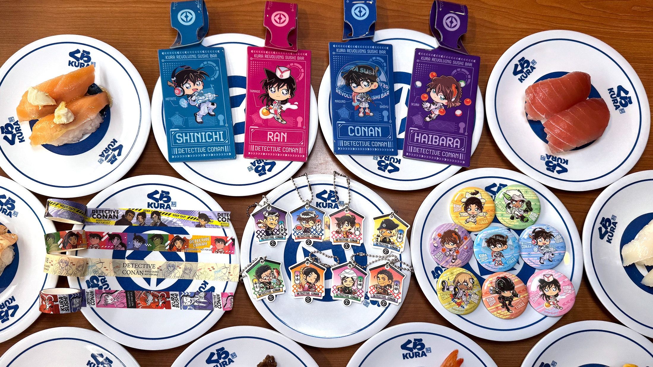 連鎖壽司店「藏壽司」與《名偵探柯南》合作，即日起至2025年7月17日推出多款聯名商品，從徽章、掛飾、紙膠帶到行李吊牌，還推出夏季限定餐點。（藏壽司提供）