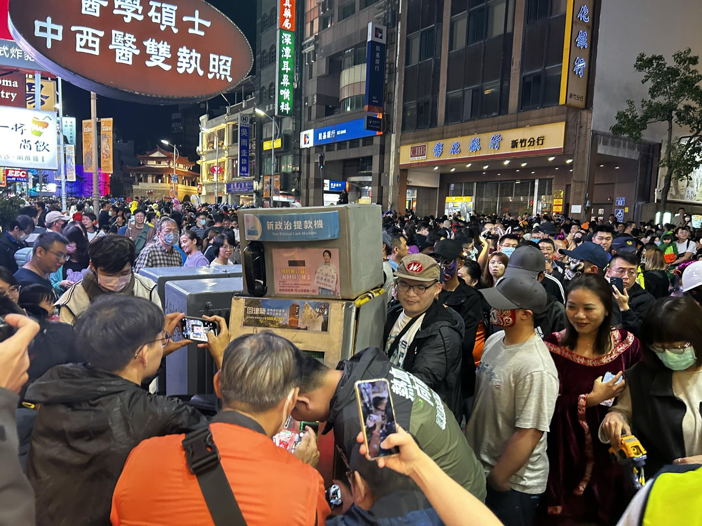 「新政治提款機」扮裝者上街遭8名臉譜男包圍,警方證實8人已依強制罪送辦,但身分不公開。(翻攝自新竹市新政治臉書)