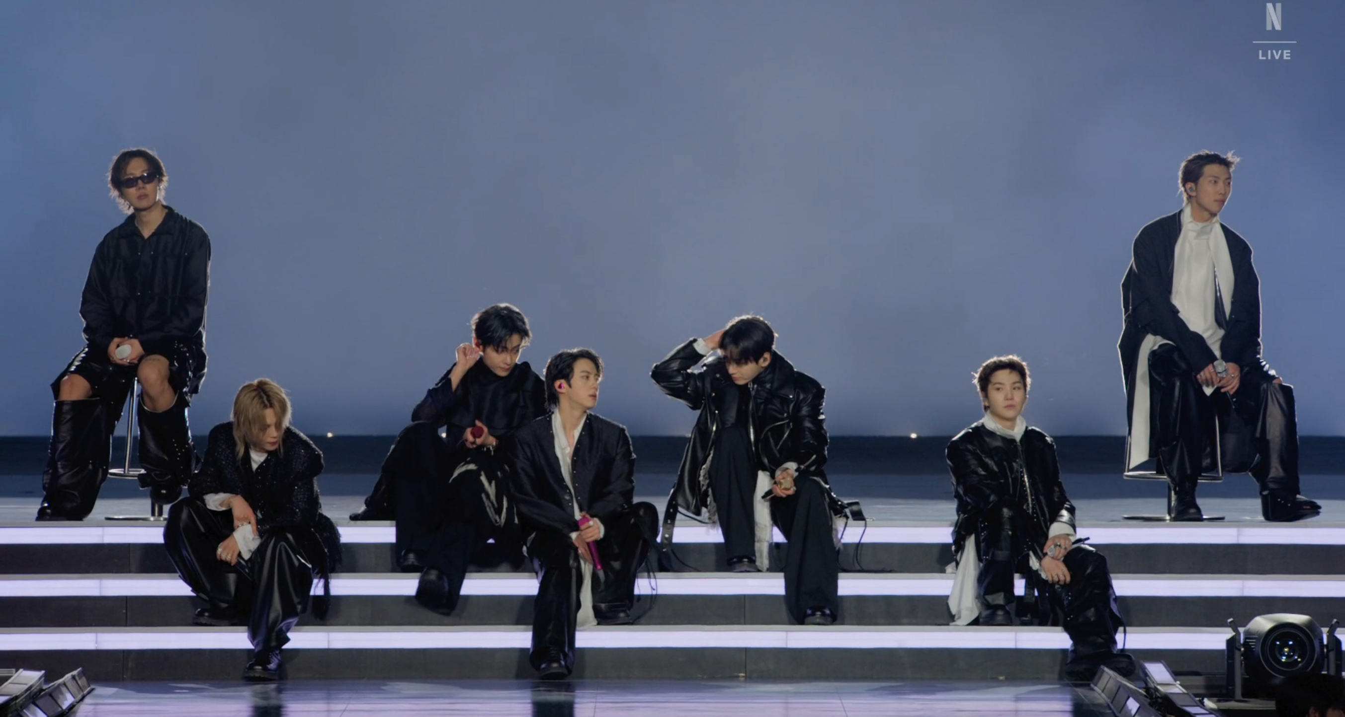 BTS今（21日）在首爾光化門廣場舉辦回歸活動，隊長RM（左一）因腳傷坐在椅子上表演。（截圖自Netflix）