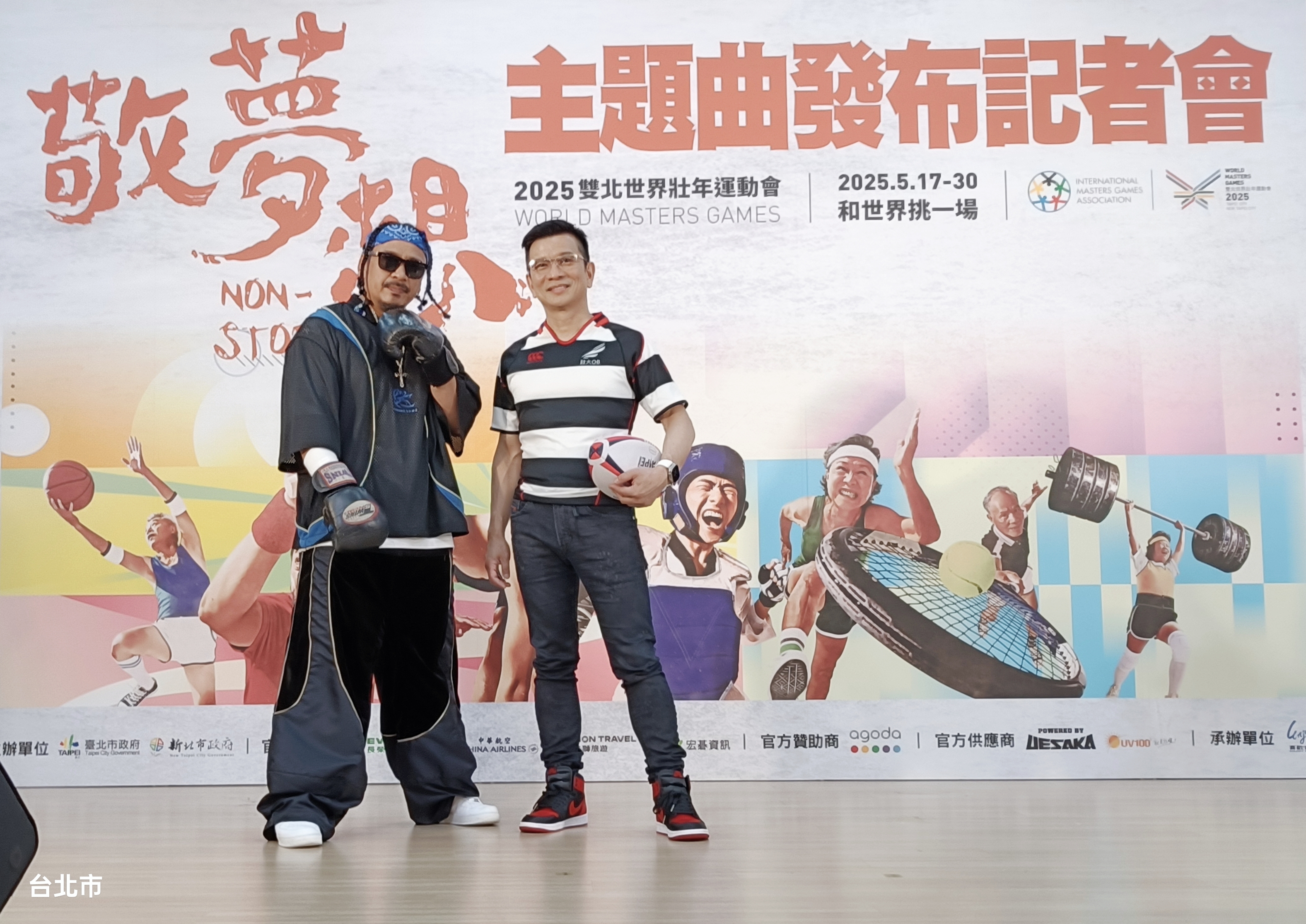 世壯運主題曲音樂統籌陳子鴻（右）特別穿上球衣出席，和主唱人葛西瓦（左）在記者會上拿起橄欖球和拳擊手套，重溫青春運動夢想。（台北市政府文化局提供）