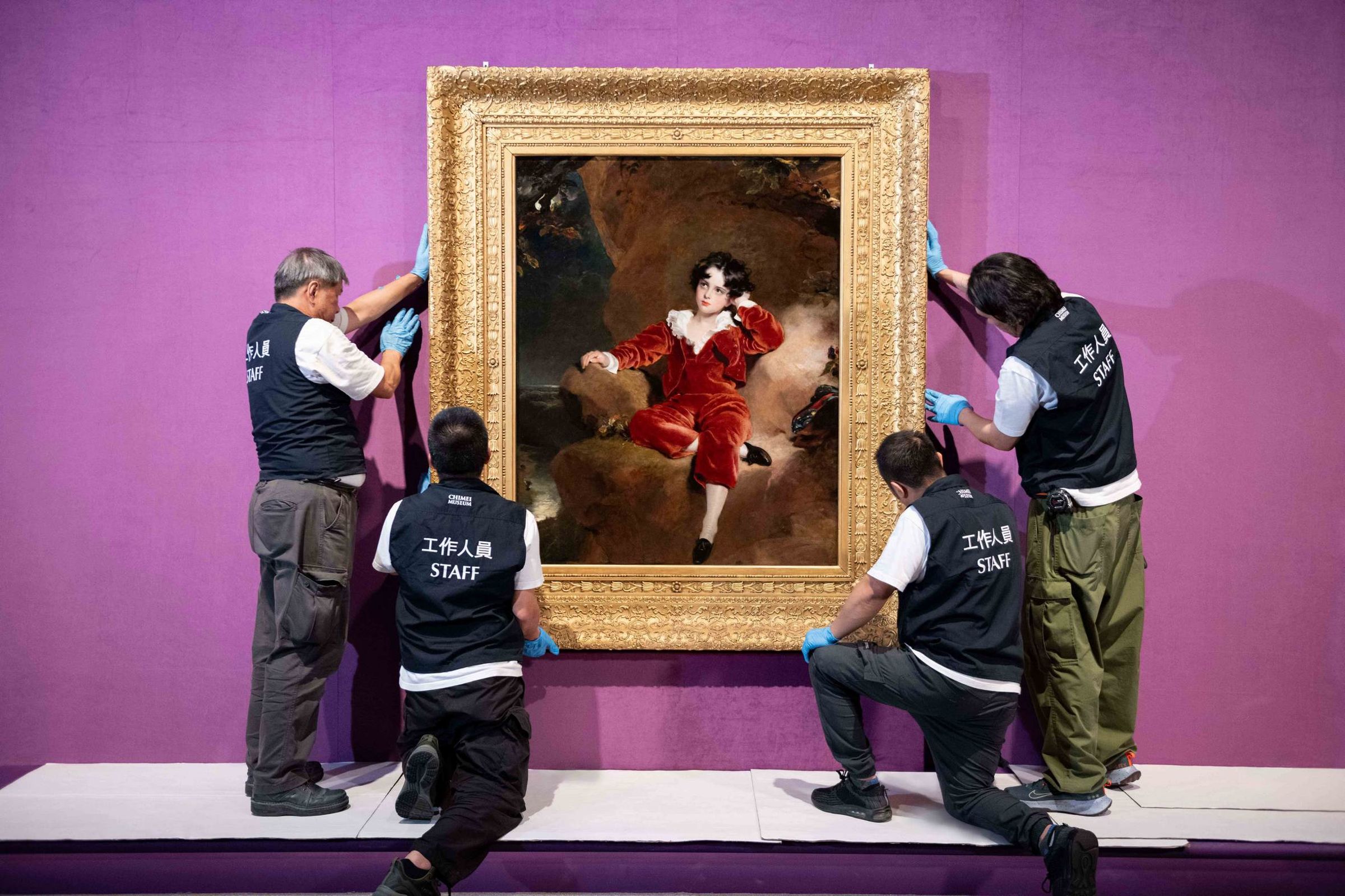 奇美博物館《英國國家藝廊珍藏展》布展過程中，工作人員將勞倫斯的作品〈查爾斯．威廉．蘭姆頓肖像〉（紅衣男孩）掛於牆上。（奇美博物館提供）