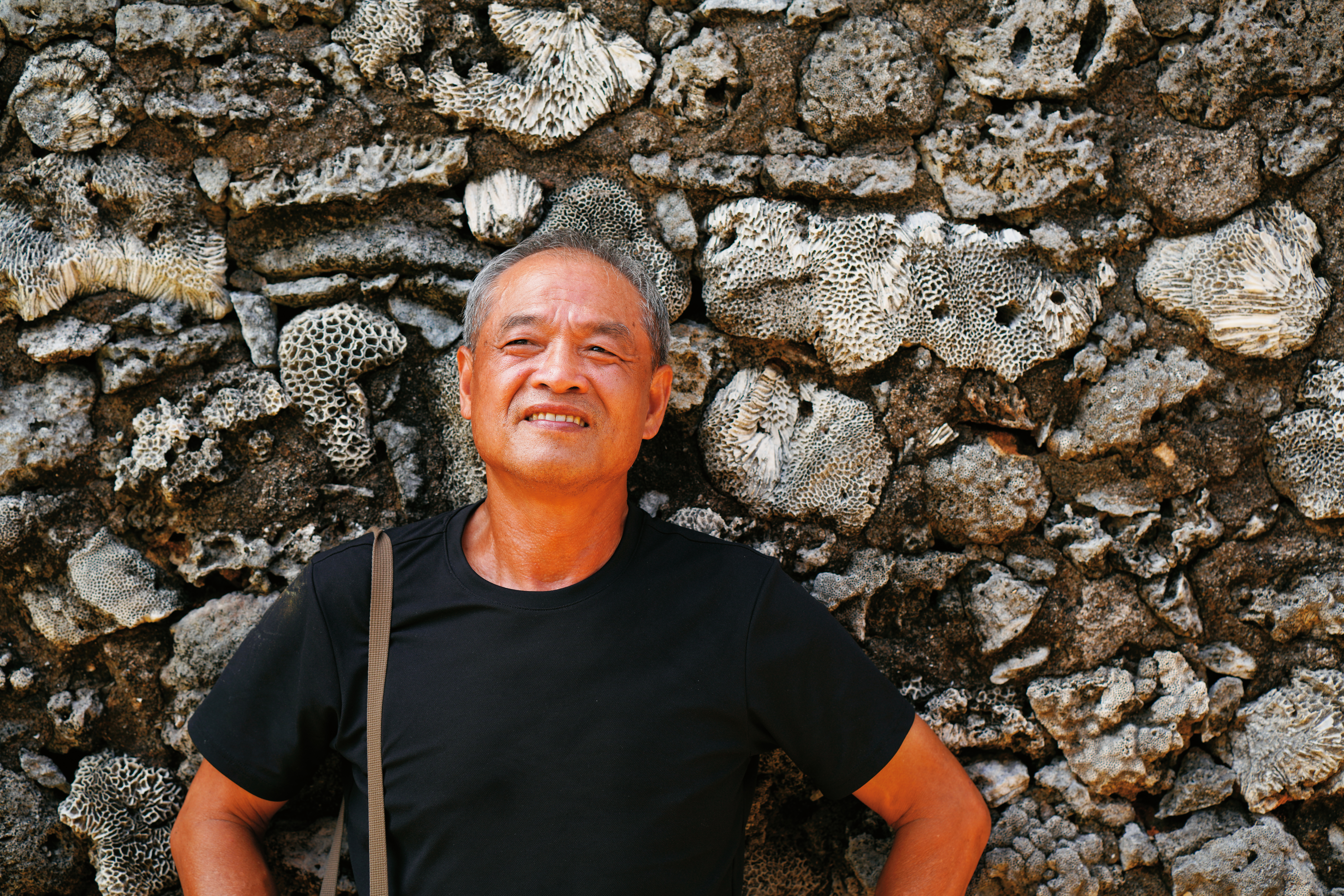 謝三泰在澎湖傳統建築的咾咕石牆前。澎湖曾是他一心逃離的地方，卻也是漂泊異鄉四十多年後想回返的原鄉。