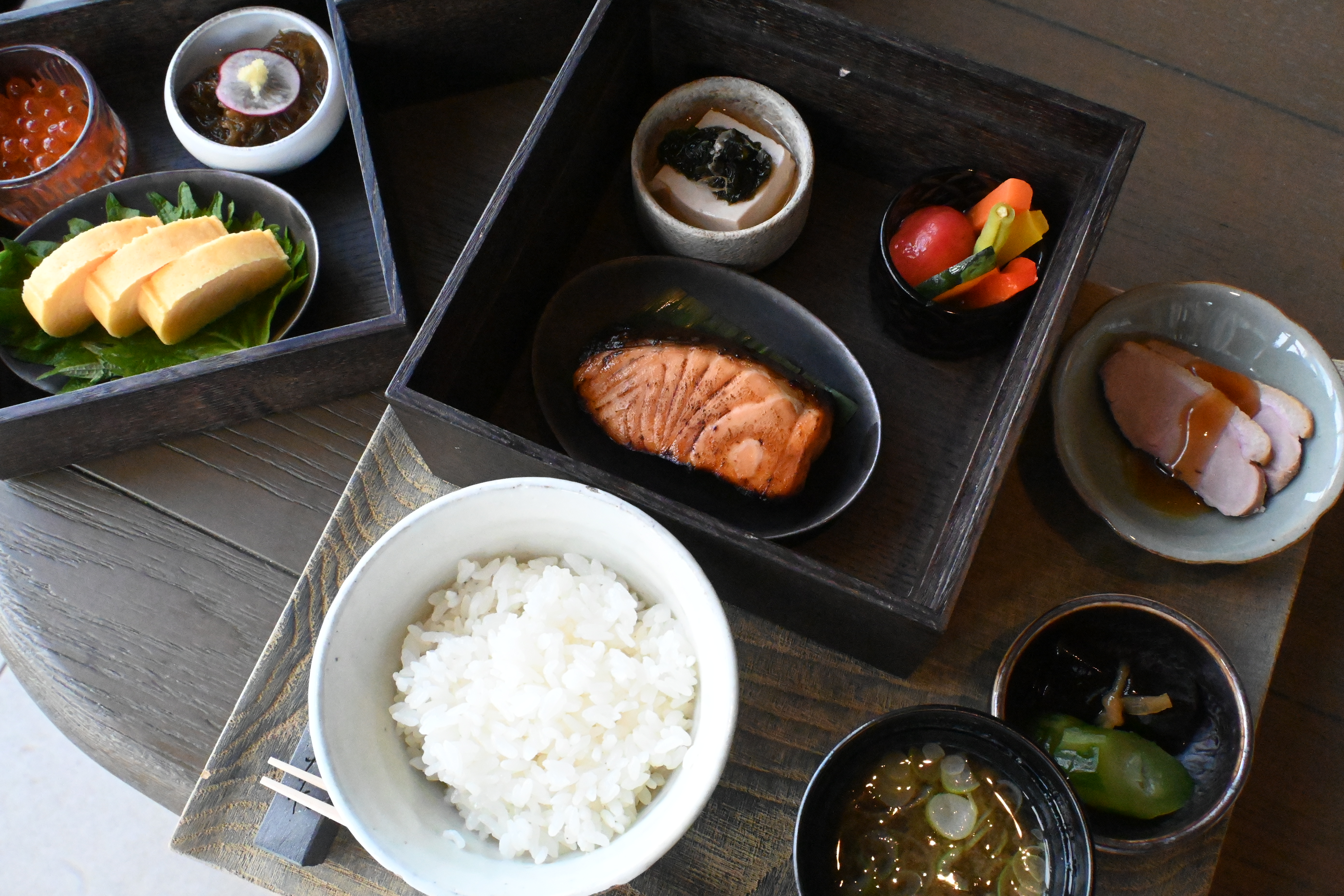 NAGI的日式早餐「Japanese」包含烤鮭魚、時令燉蔬菜、日式玉子燒搭配蘿蔔泥、花生豆腐佐柴魚片、黑醋海藻（もずく）、醃漬蔬菜等多道小菜，搭配白飯與味噌湯。（日幣8,000元／份，約NT$1516）