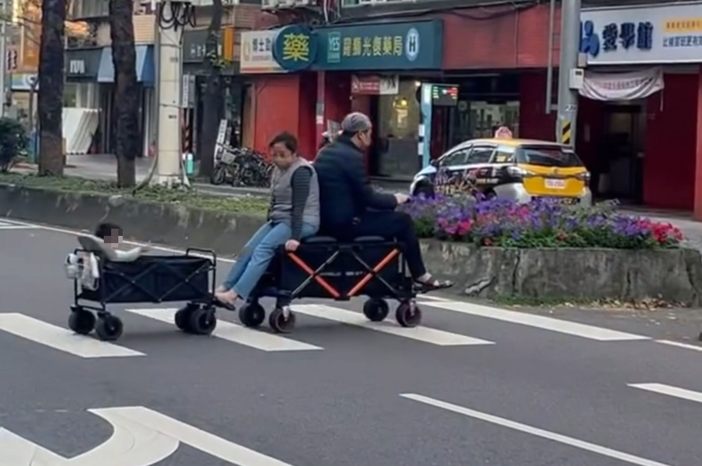 一對男女日前在台北街頭利用電動手拉車串接手拉車方式，載著孩童過街，引發網友熱議。（翻攝自96s_kai@Threads ）

