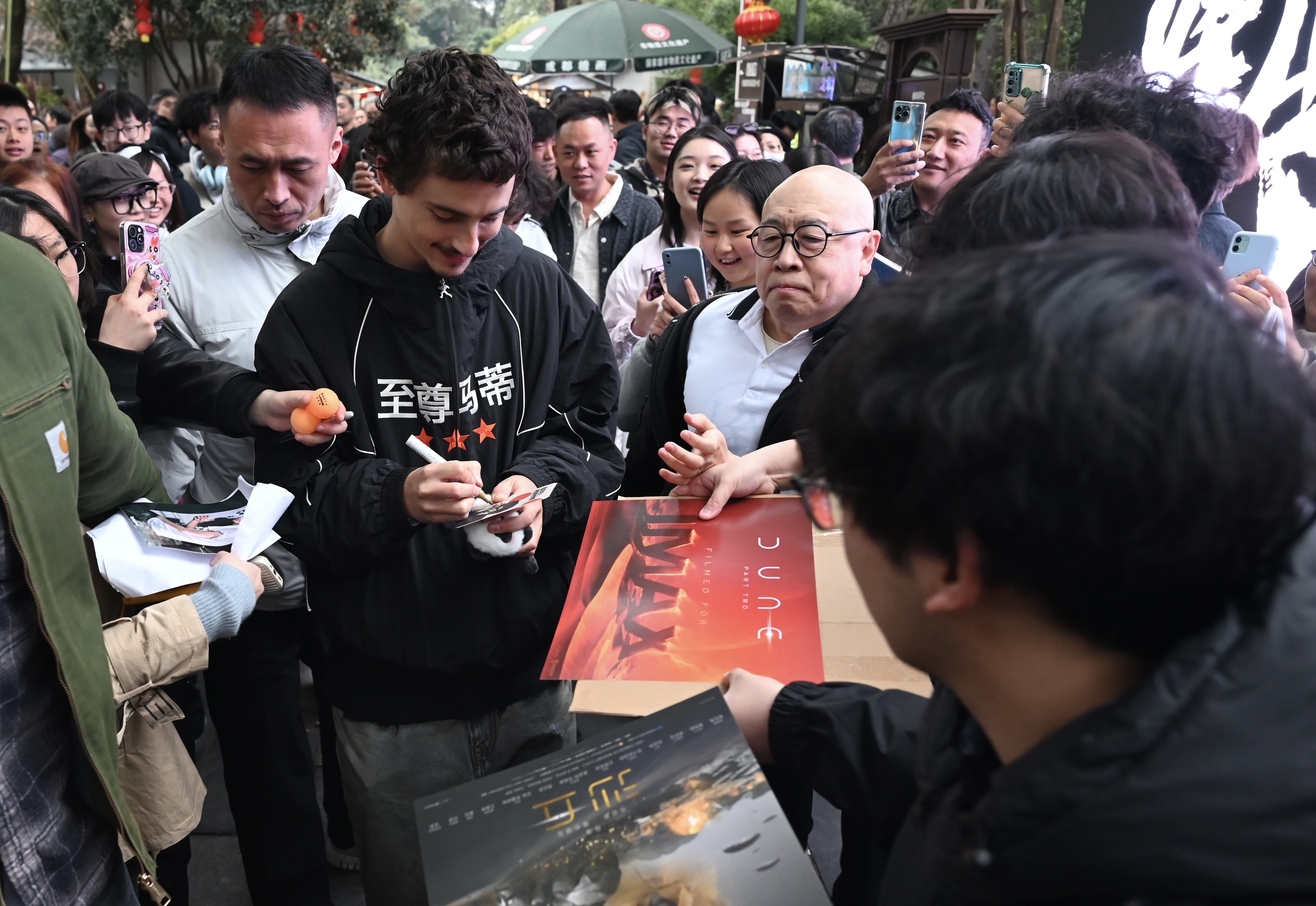 提摩西夏勒梅（左）刻意穿上印有片名的帽T，在成都路上亂竄，引發路人圍觀。（東方IC）
