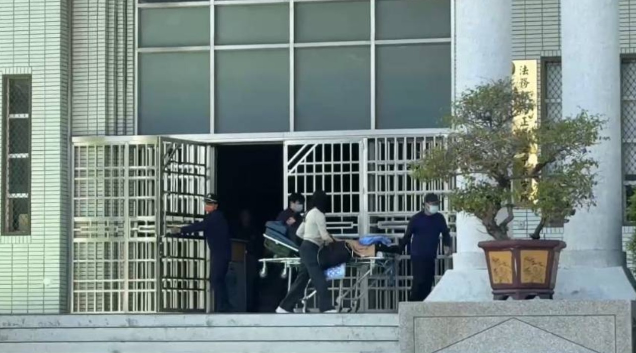 罹患重病的林明佐躺在擔架上，由管理員和家屬推出台中看守所。