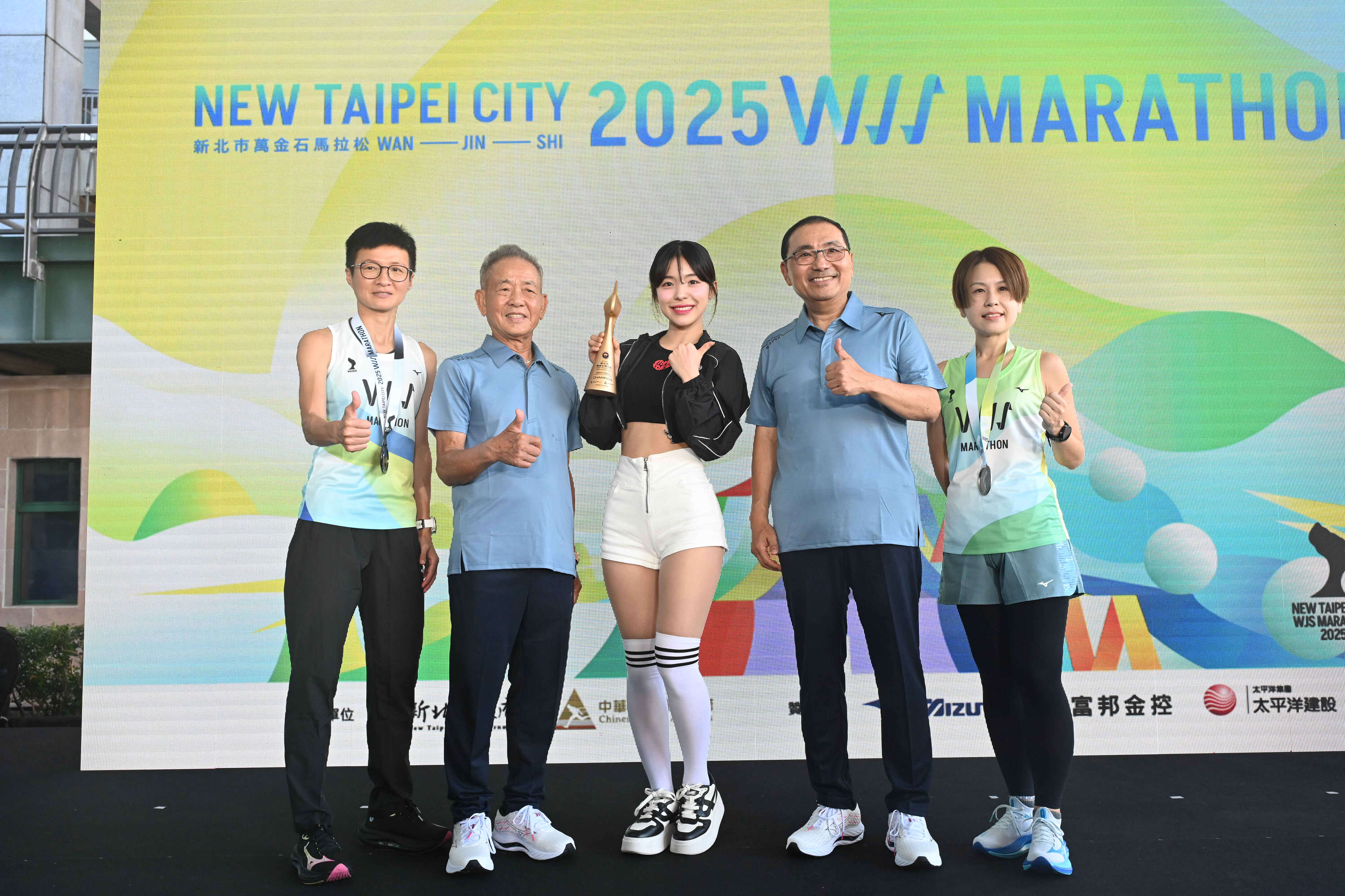 李多慧(中)及跑者一同展示紀念跑衣、完賽獎牌及火炬流線形獎盃。(新北市政府提供)