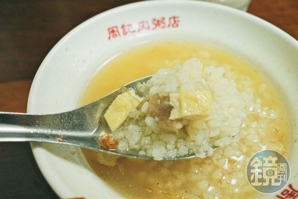 周記的肉粥不同於一般稀飯或軟綿的廣東粥，店家以生米熬煮，保持米粒分明宛如高湯泡飯的口感。湯頭是用大骨熬製，並加入油豆腐碎、碎肉焿、油蔥酥和蝦米提味。（鏡週刊提供）