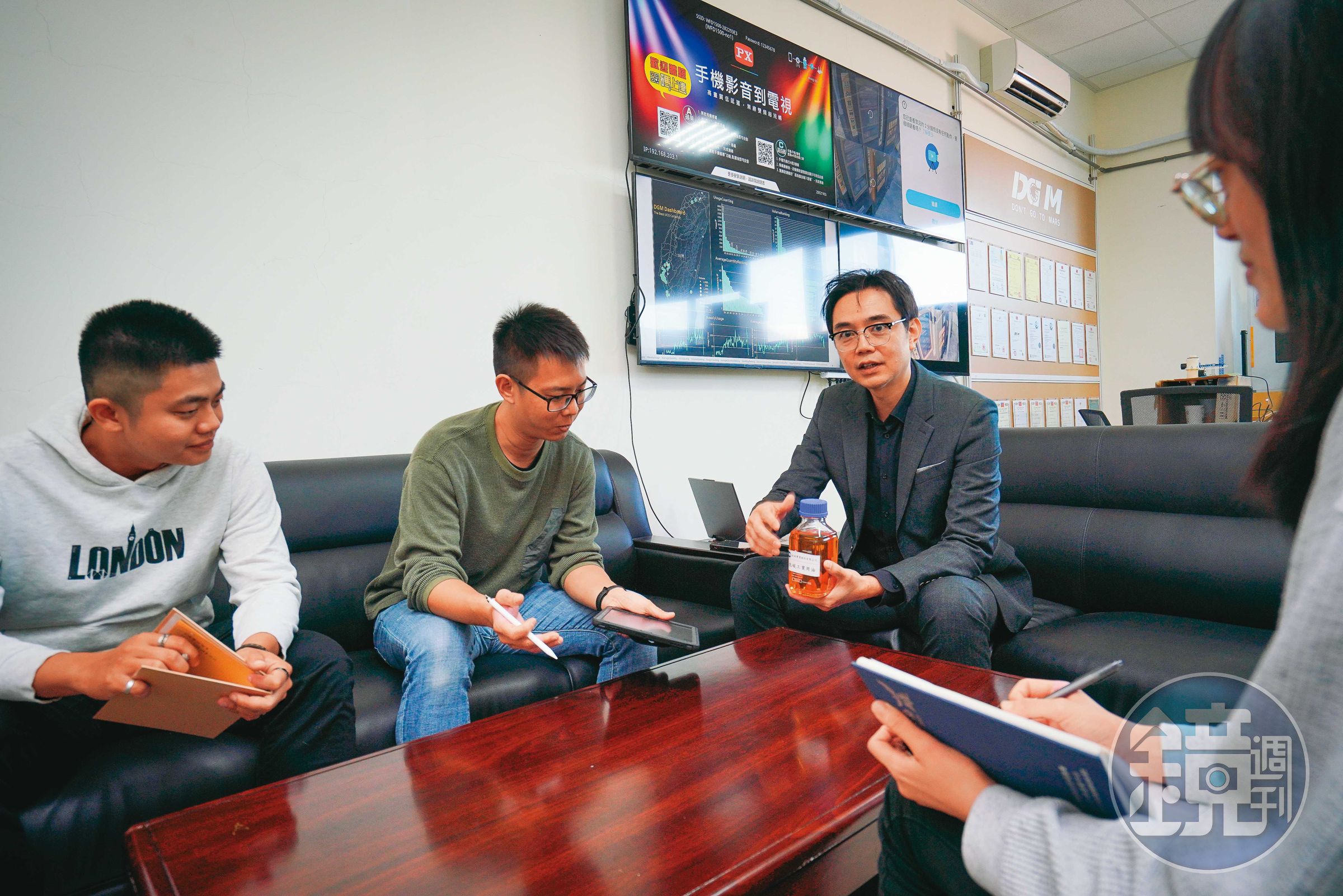 林修安（右二）與同事討論廢食用油回收狀況，背後的電視牆就是設立在各地的智慧廢食用油回收系統的戰情資訊螢幕。