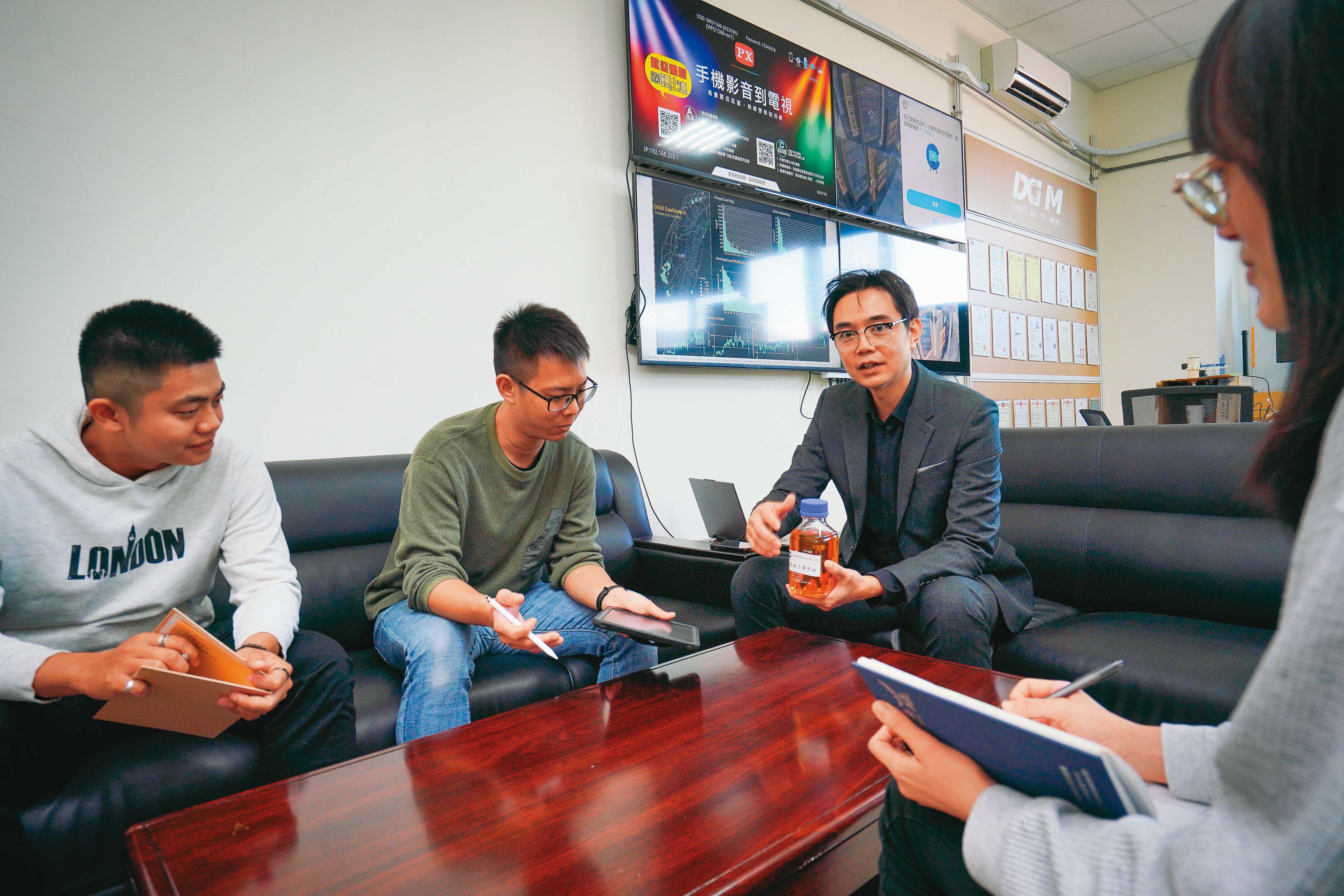 林修安（右二）與同事討論廢食用油回收狀況，背後的電視牆就是設立在各地的智慧廢食用油回收系統的戰情資訊螢幕。