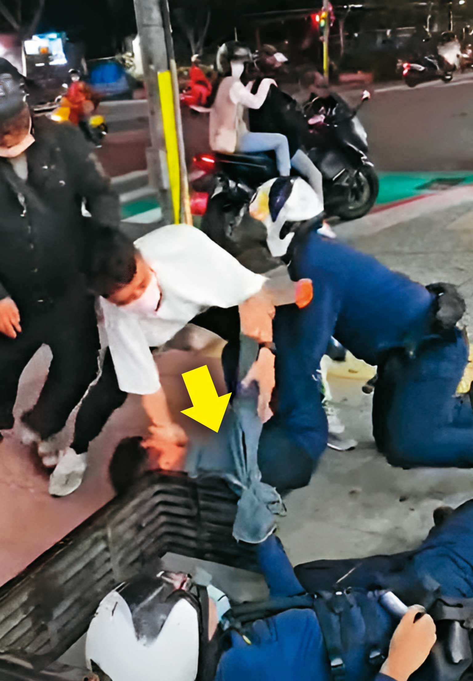 黃先生（箭頭處）被員警推倒在人行道上，一旁的民眾也上前協助員警逮人。（翻攝畫面）