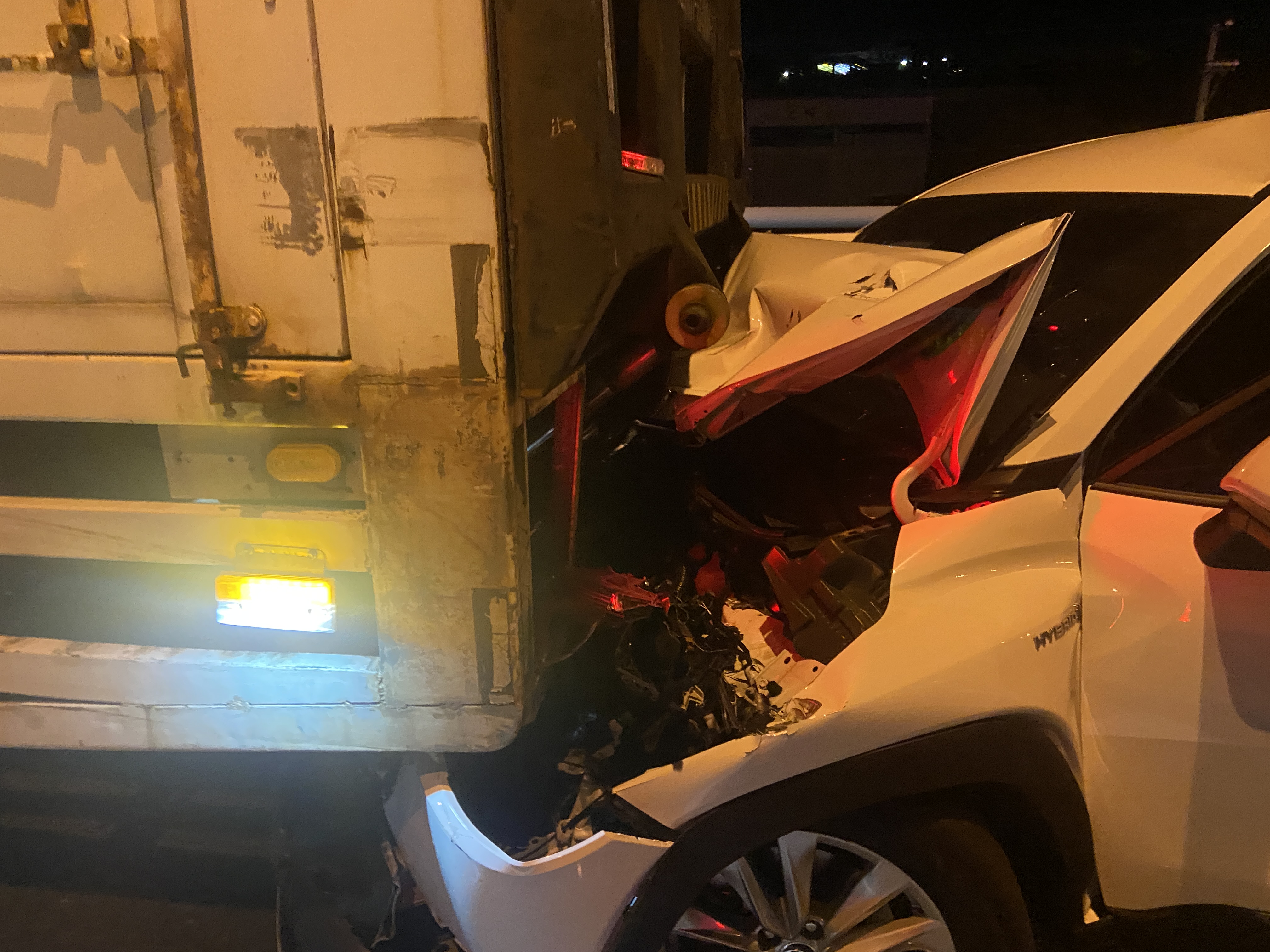 車禍事故中1部轎車被夾在2輛大貨車間,車頭嚴重毀損,駕駛輕傷送醫。(翻攝畫面)
