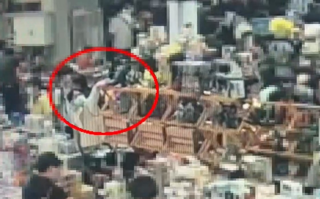 一名戴眼鏡男子趁人潮眾多，伸手拉哥吉拉公仔的尾巴，隨即將公仔偷走。（翻攝畫面）