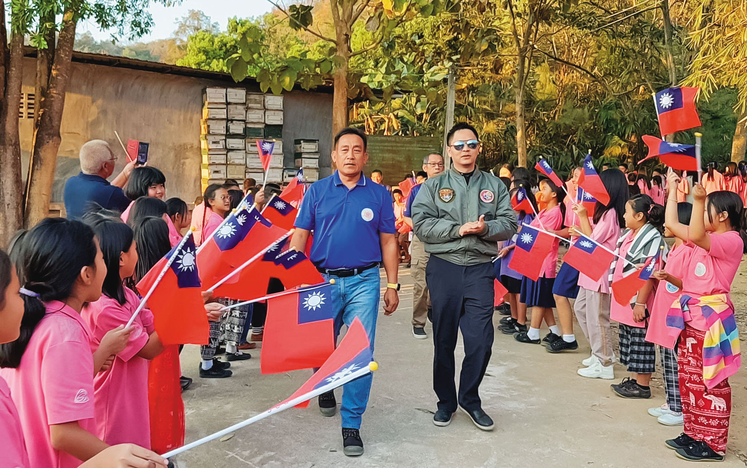 多次自費到泰北為孤兒做公益表演的黃信凱（右），在當地受到小朋友拿國旗夾道歡迎。（黃信凱提供）