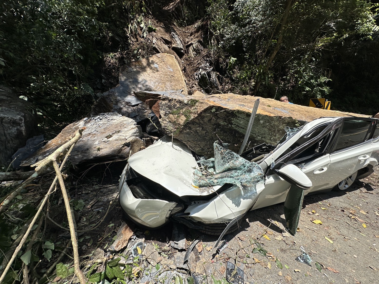 新北市烏來山區今日上午發生落石坍方，造成一部停放路旁的自小客車遭巨石砸中，所幸駕駛不在車上。（翻攝畫面）