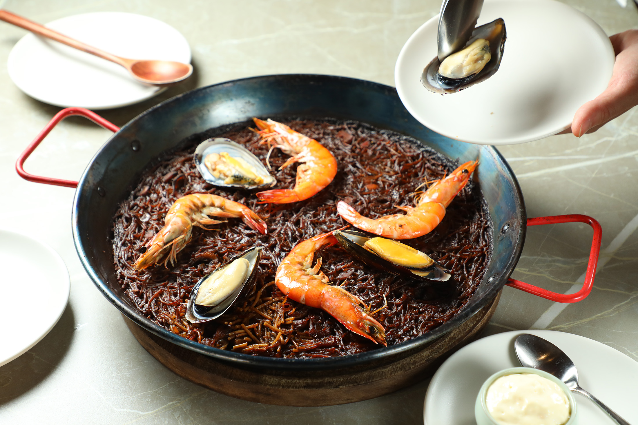 「ORIGEN純正西班牙餐廳」的「西班牙海鮮短麵」選用特製微空心短麵，吸飽海鮮高湯後高溫烤出酥脆焦香，搭配蒜味美乃滋，重現瓦倫西亞的經典風味。（1,680元／份）