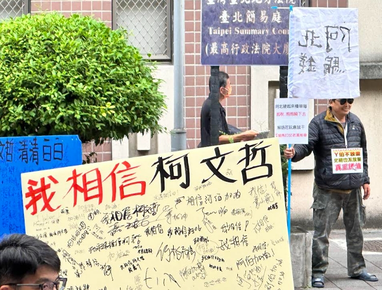 柯文哲的支持者手持「相信柯文哲標語」與對街持「阿北騙錢」的男子較勁。