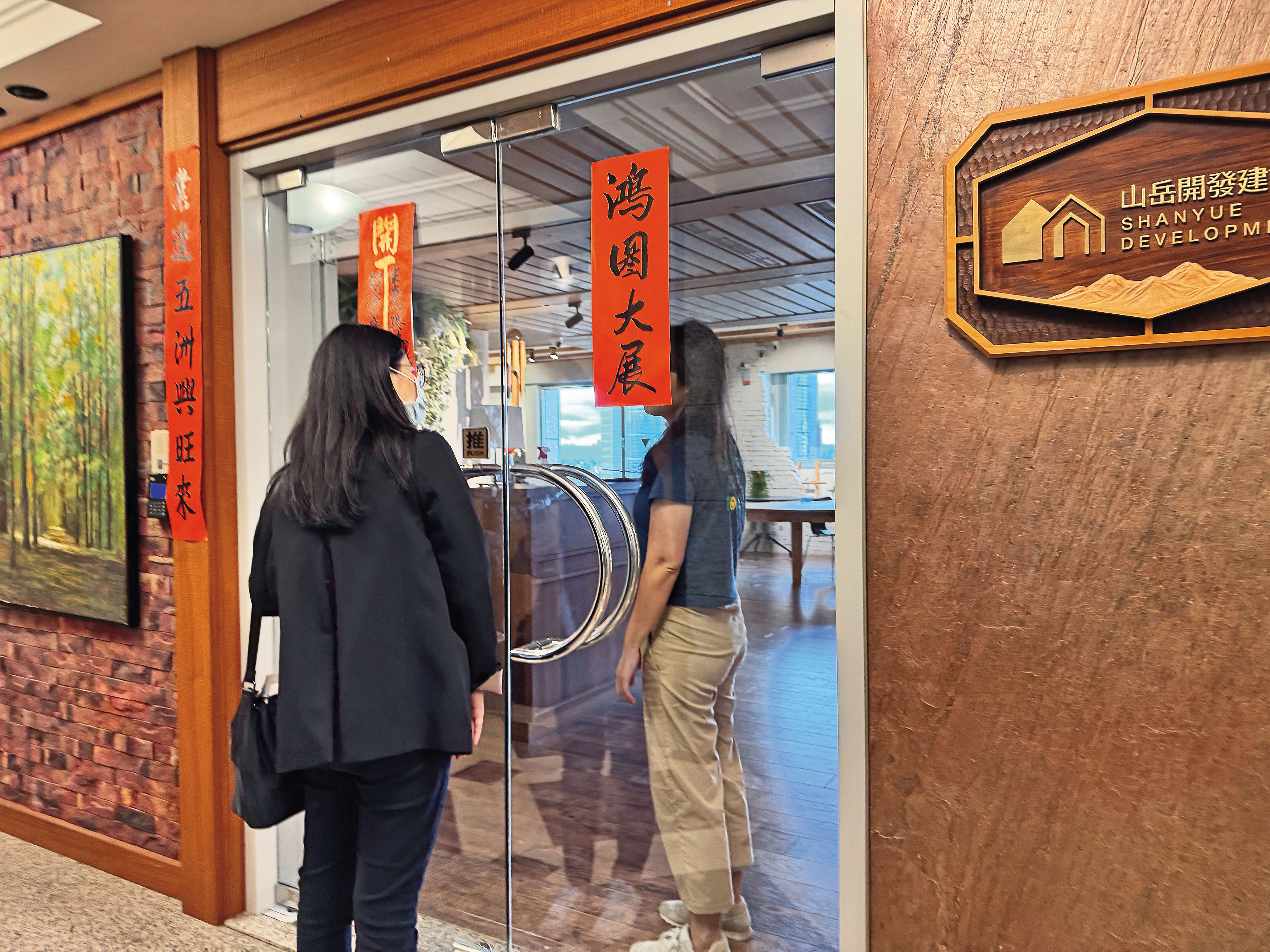 本刊前往山岳建設查證汐止都更爭議,一名女性員工(右)透過上鎖的玻璃門縫隙表示不回應。