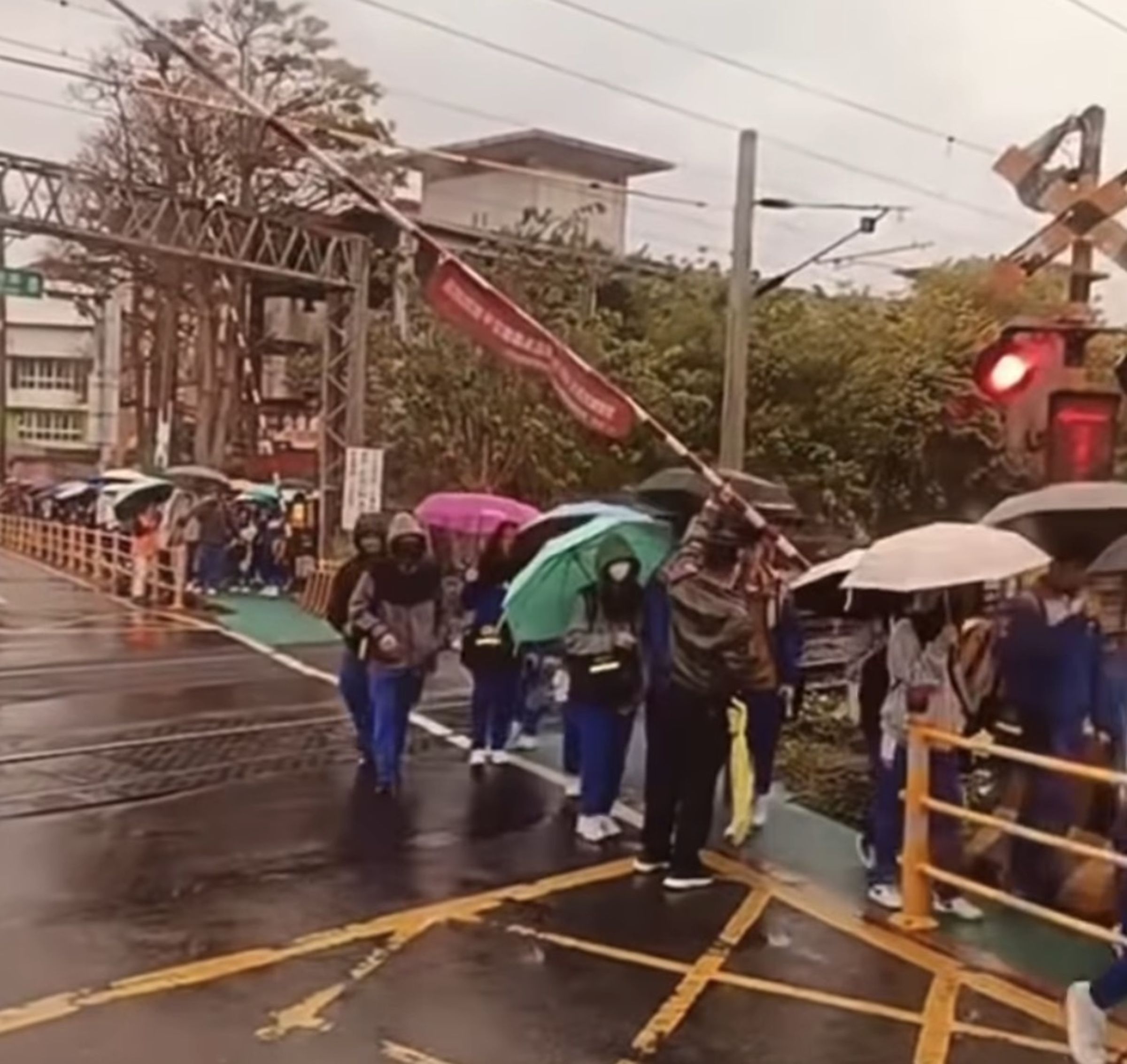 平交道警鈴大響，一旁校方人員不但沒有阻止學生通過反而還「幫扛柵欄」，畫面讓網友怒了！（圖：爆料公社）
