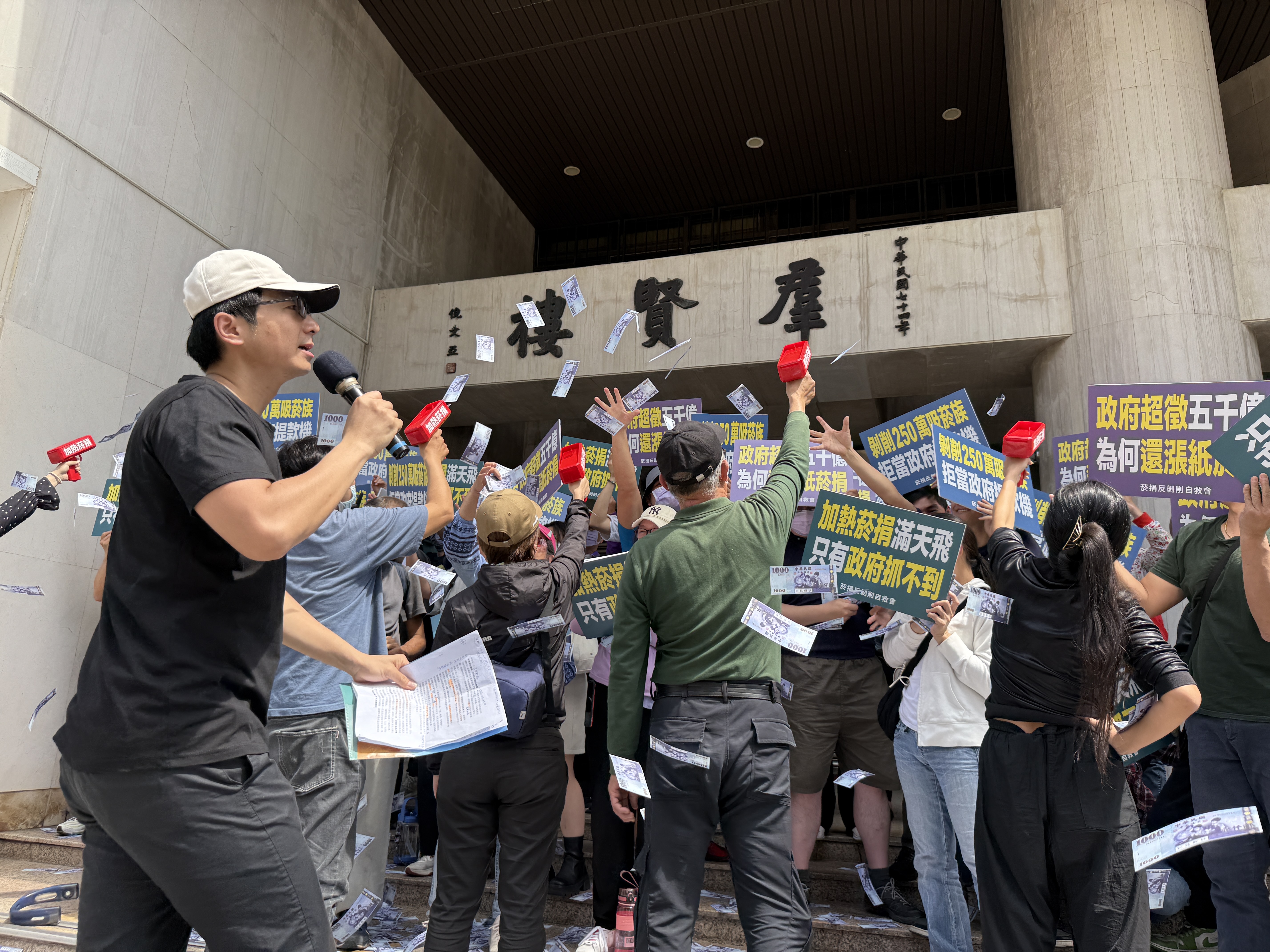 陳情的吸菸族氣憤地以玩具鈔票手槍噴灑鈔票滿天飛舞，嘲諷政府蒙上眼罩綁住雙手，才會抓不到既有可徵的菸捐。（菸捐反剝削自救會提供）